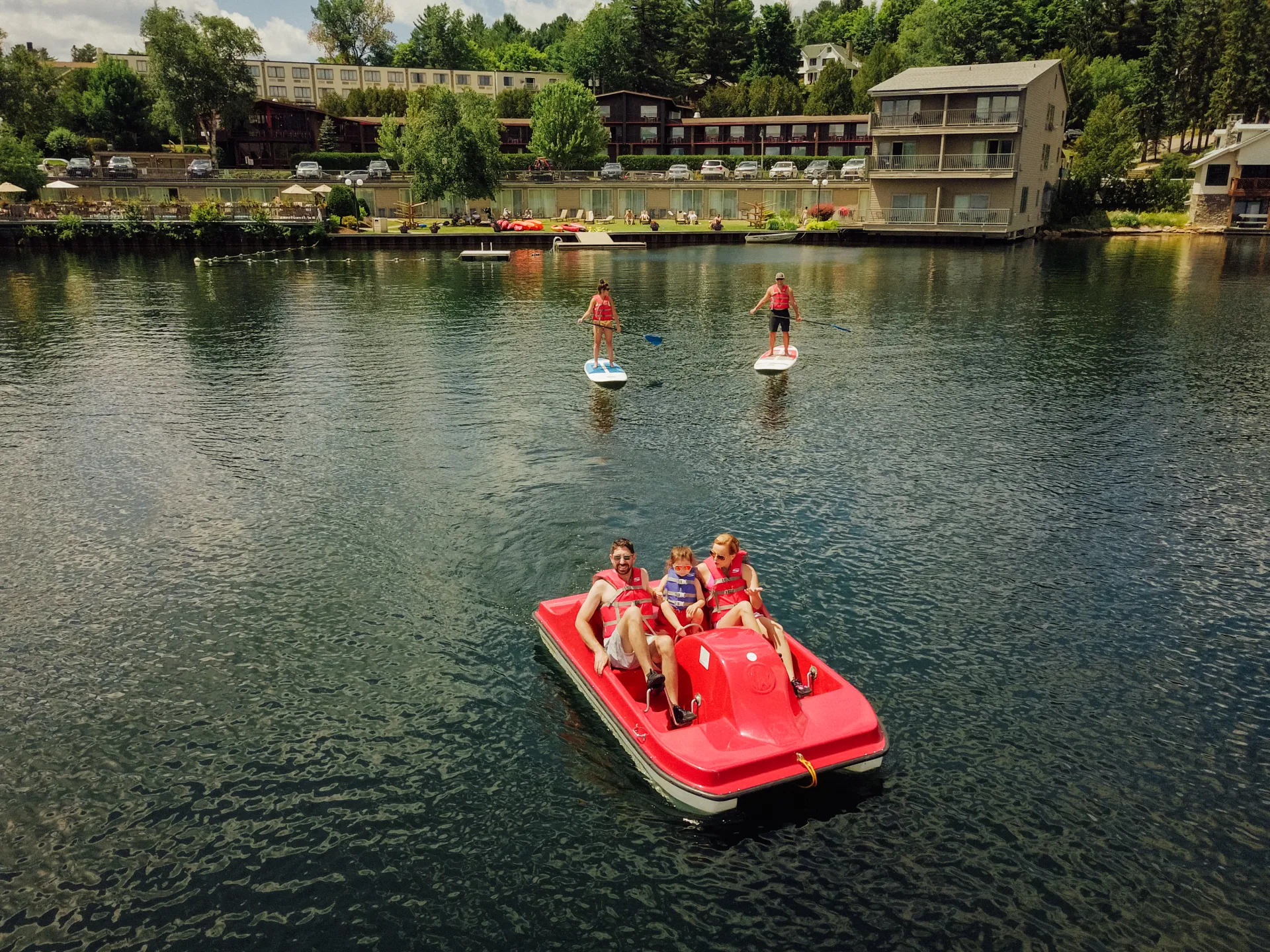 Family in red peddle boat on lake with other paddlers and people on lakeshore with hotels in background