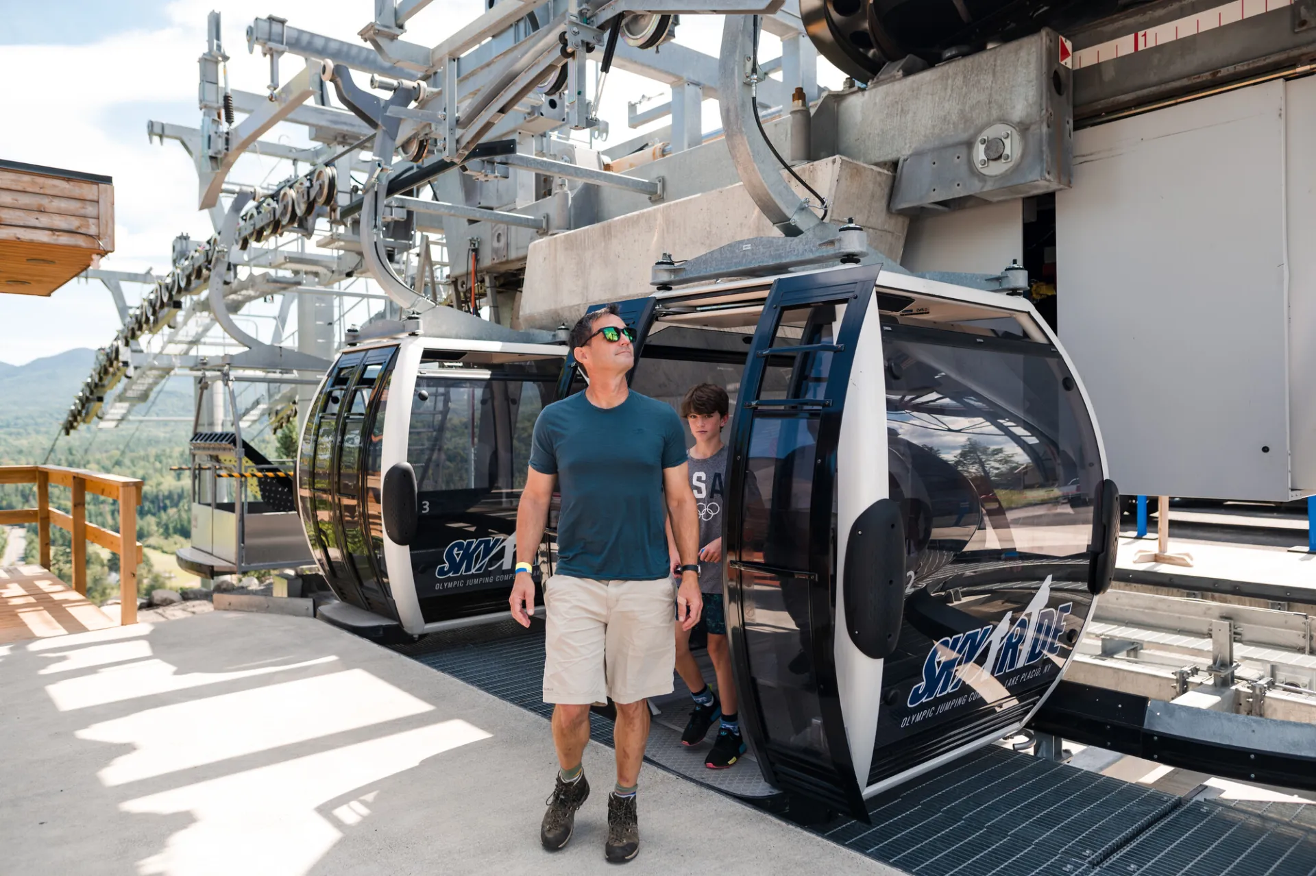 Man steps out of gondola looking around wearing t-shirt, shorts, and sunglasses