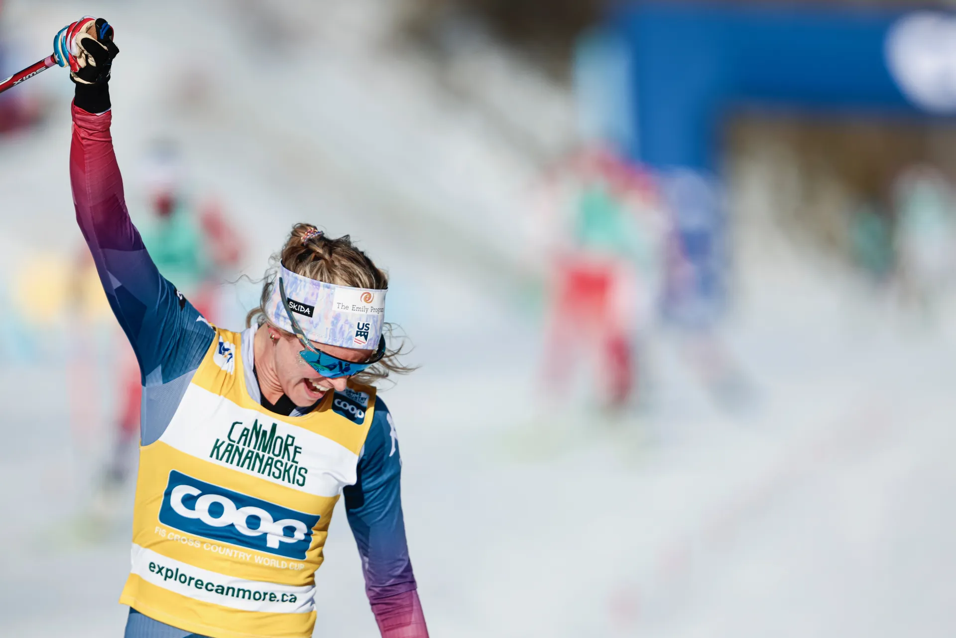 Cross-country ski racer Jessie Diggins in race gear celebrating at finish line with arm in the air