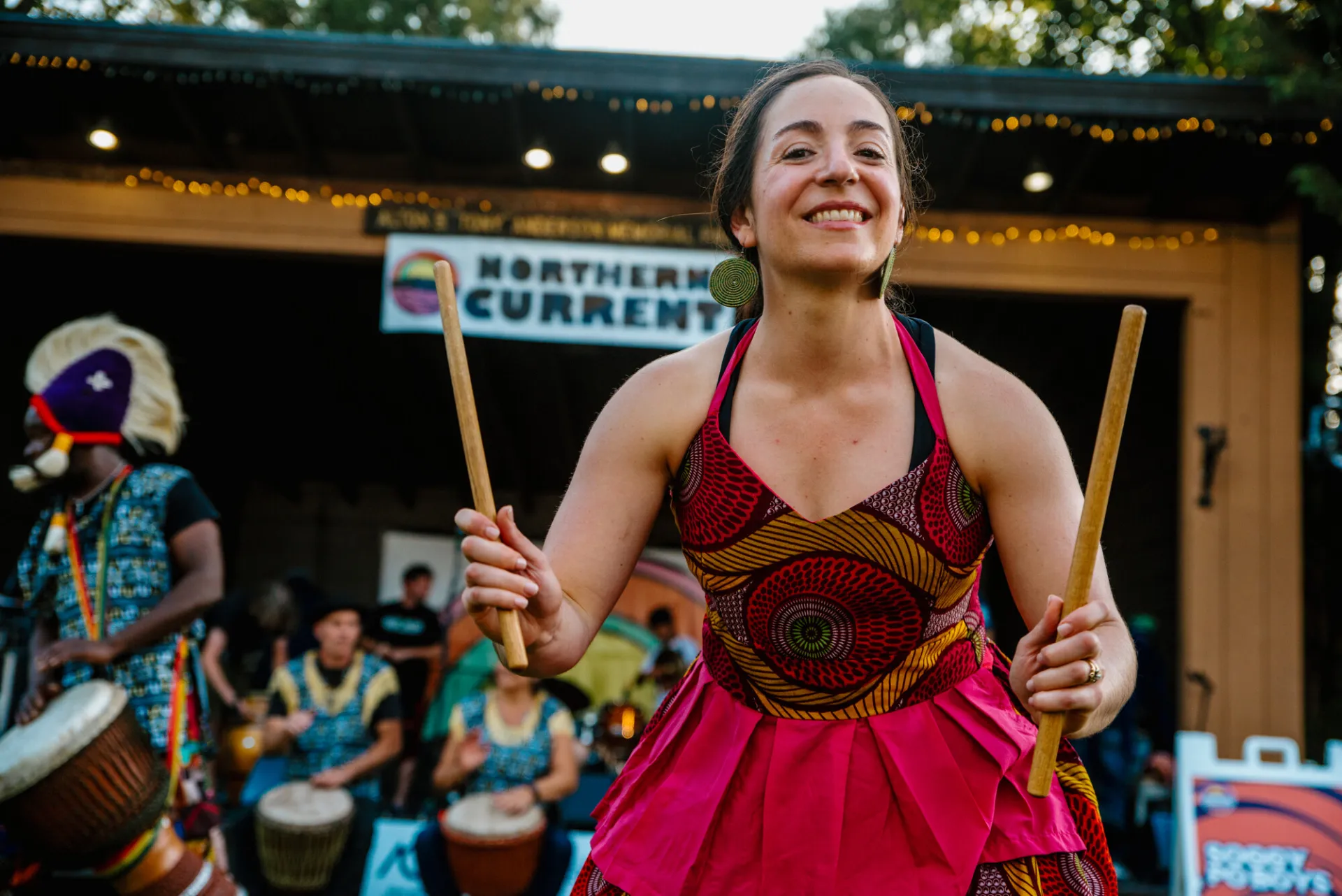 A friendly drummer in a colorful dress smiles into the crowd