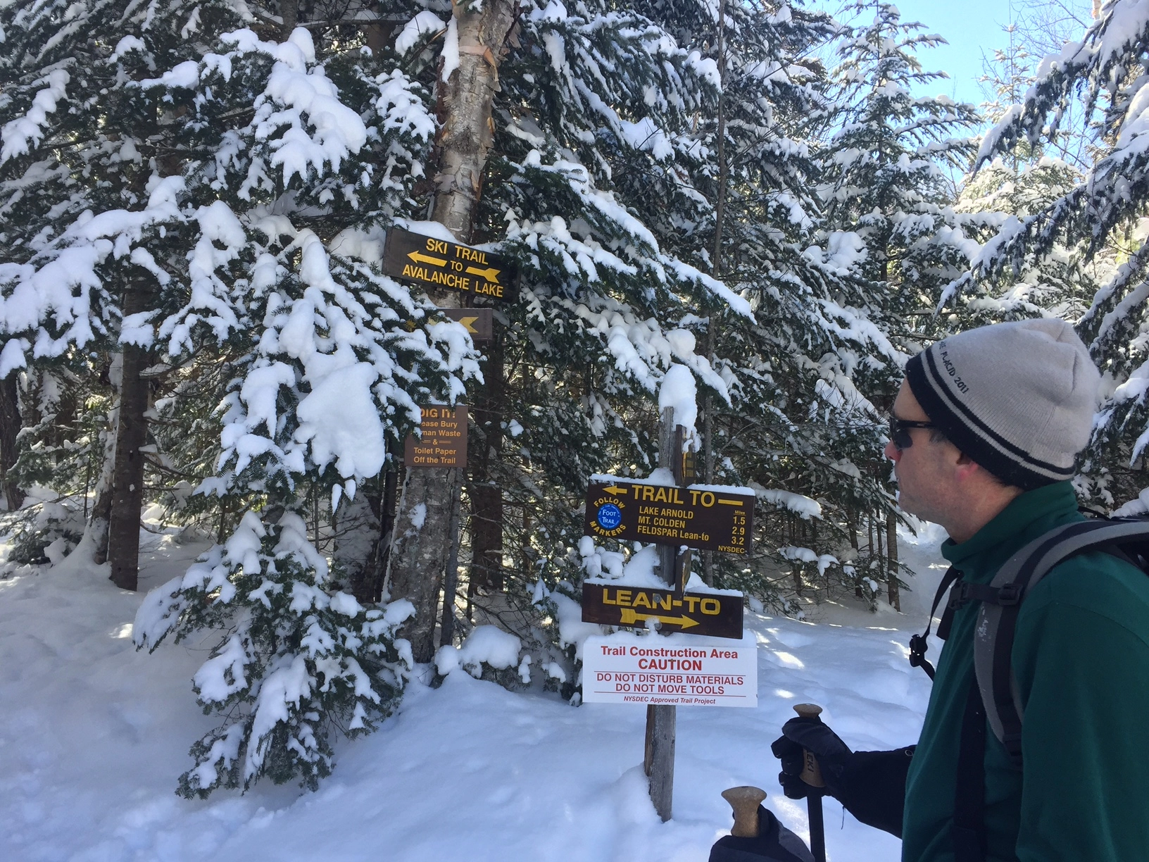 A hiker looking at wooden trail signs in the winter