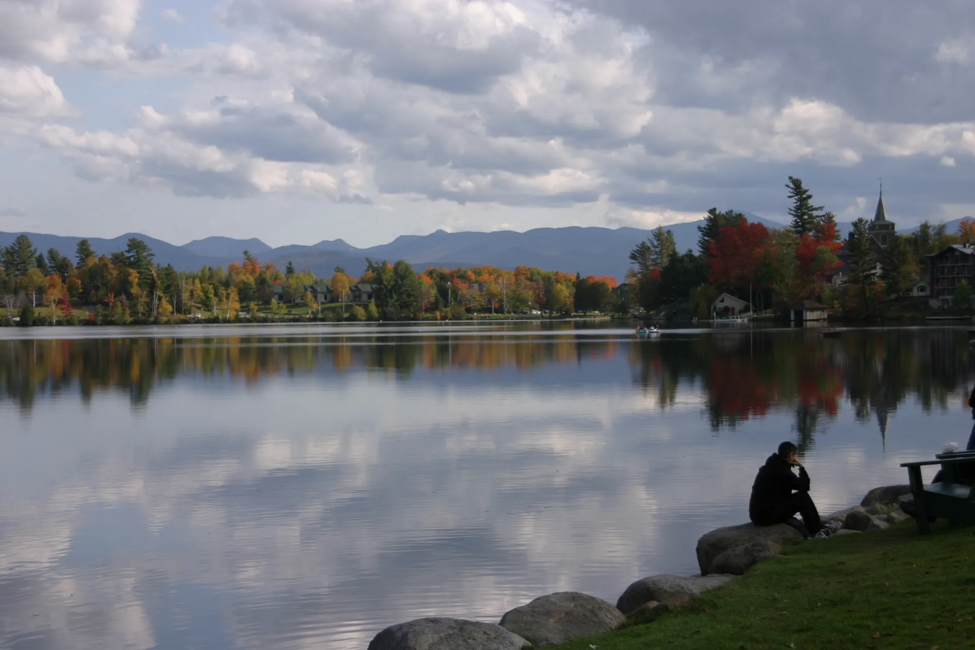 A person sits on a rock by the smooth waters in the fall.
