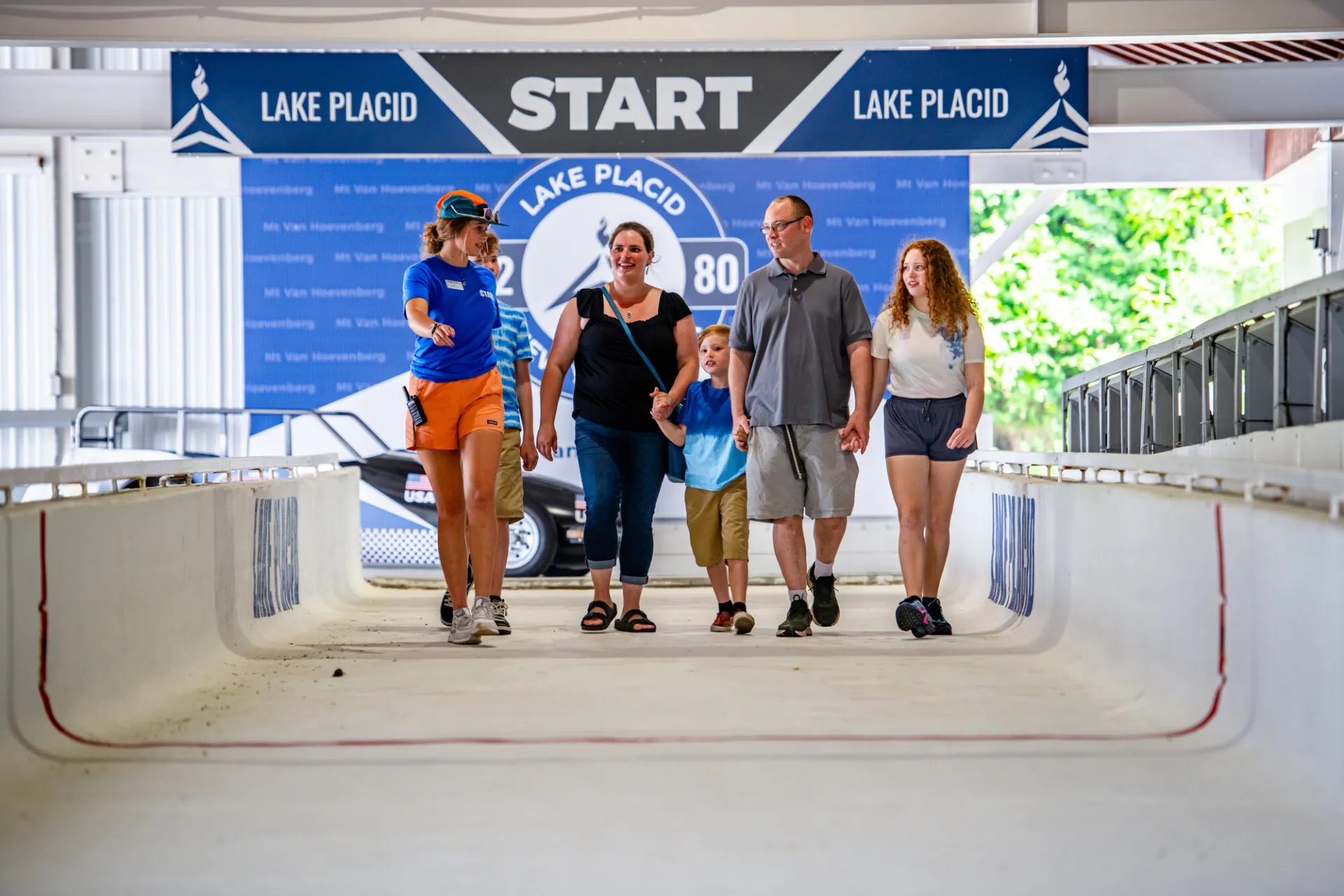 Mother, father, daughter, and two sons follow tour guide at start line of Mt Van Hoevenberg bobsled track