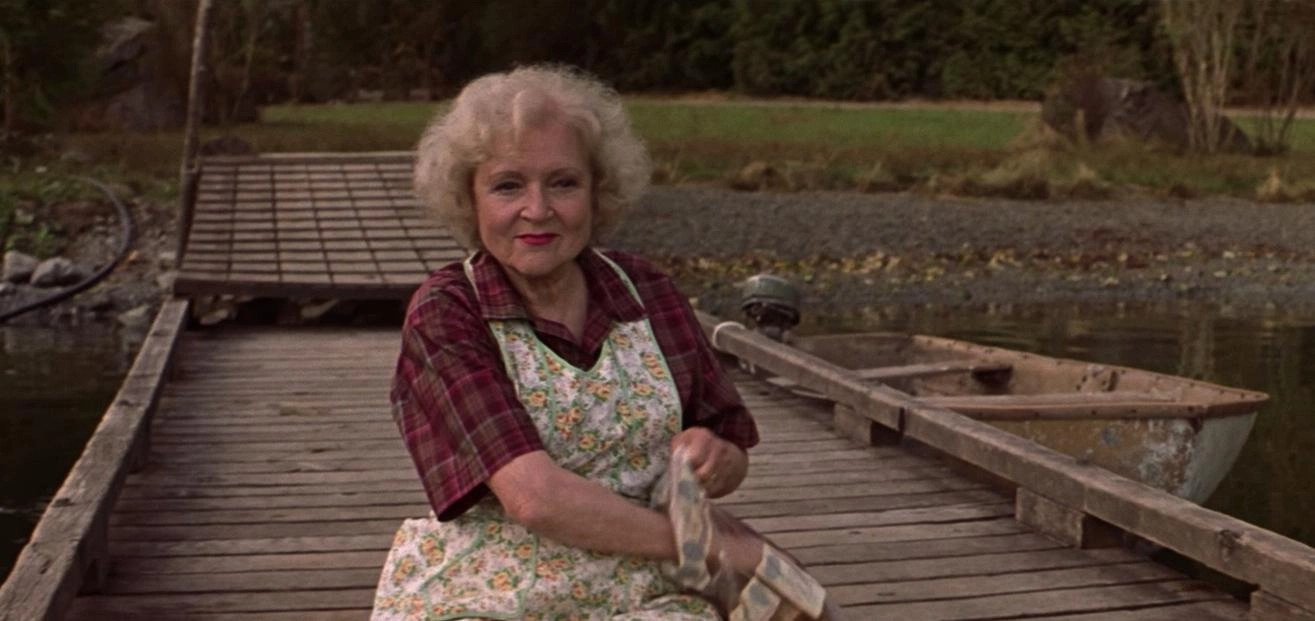 A friendly-looking elderly lady smiles gently while sitting on the end of a dock.