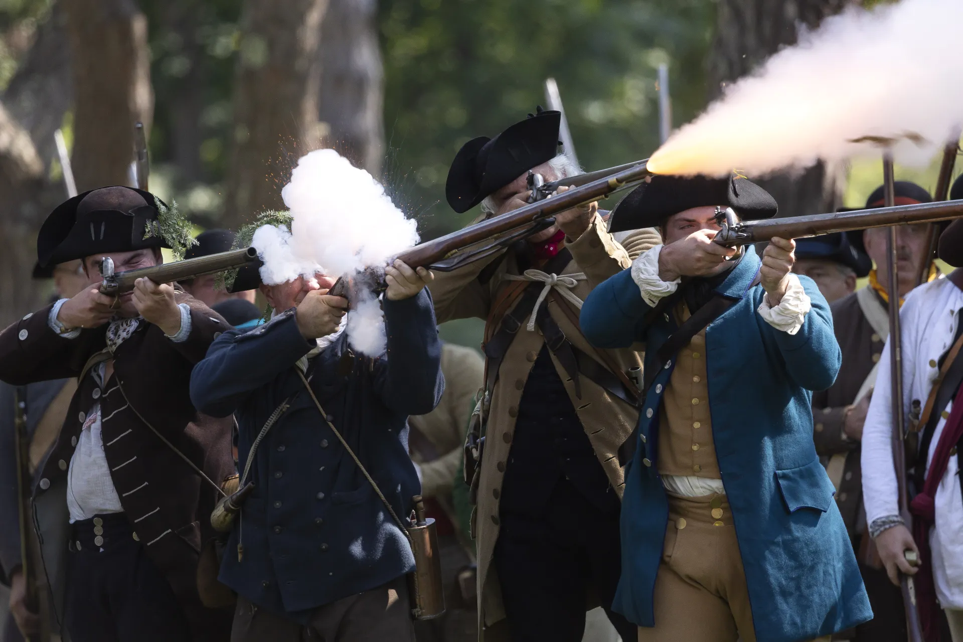 Minute men fire muskets with a puff of smoke and embers flying from one of the riffles.