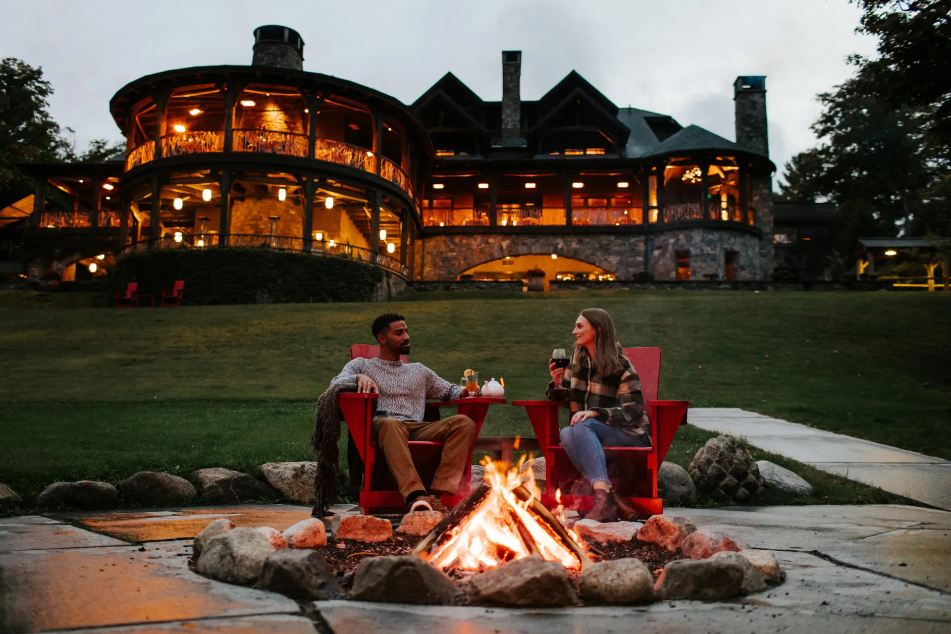 A man and woman enjoy wine at a fireplace. 