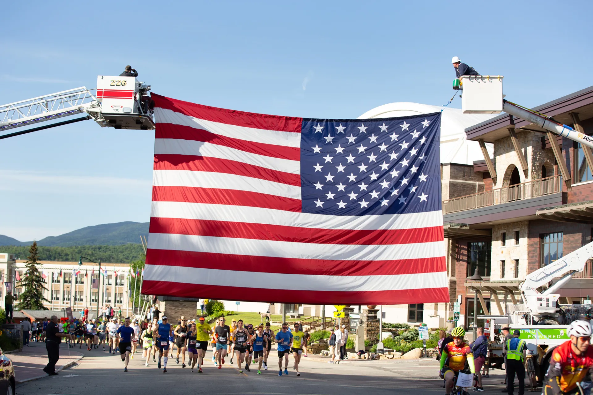 Two cranes hold up a large American flag over a marathon route through town.