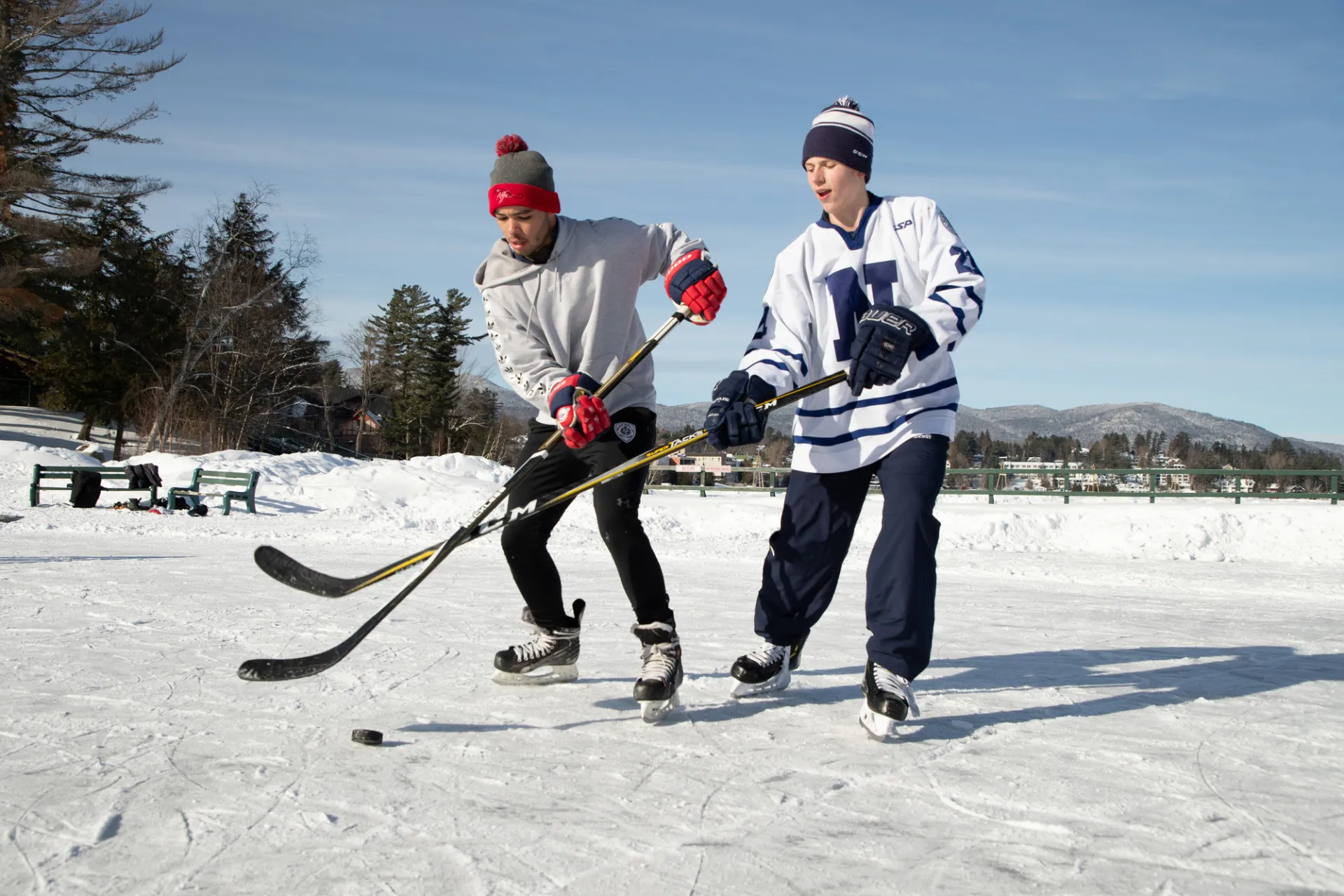 Two kids play ice hockey on a frozen lake