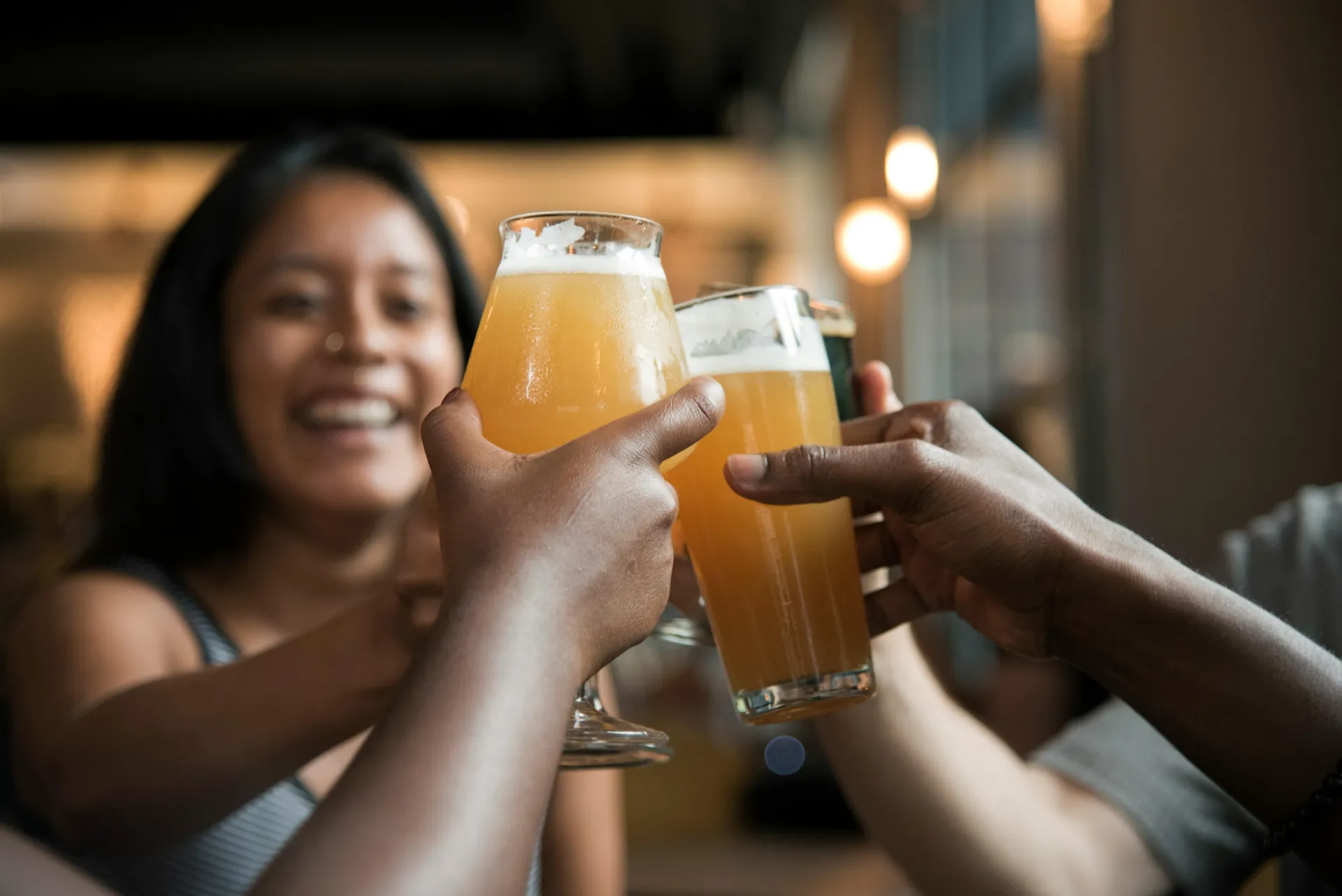 Stock image of woman raising glass of beer smiling and arms from people off screen also raising arms in cheers