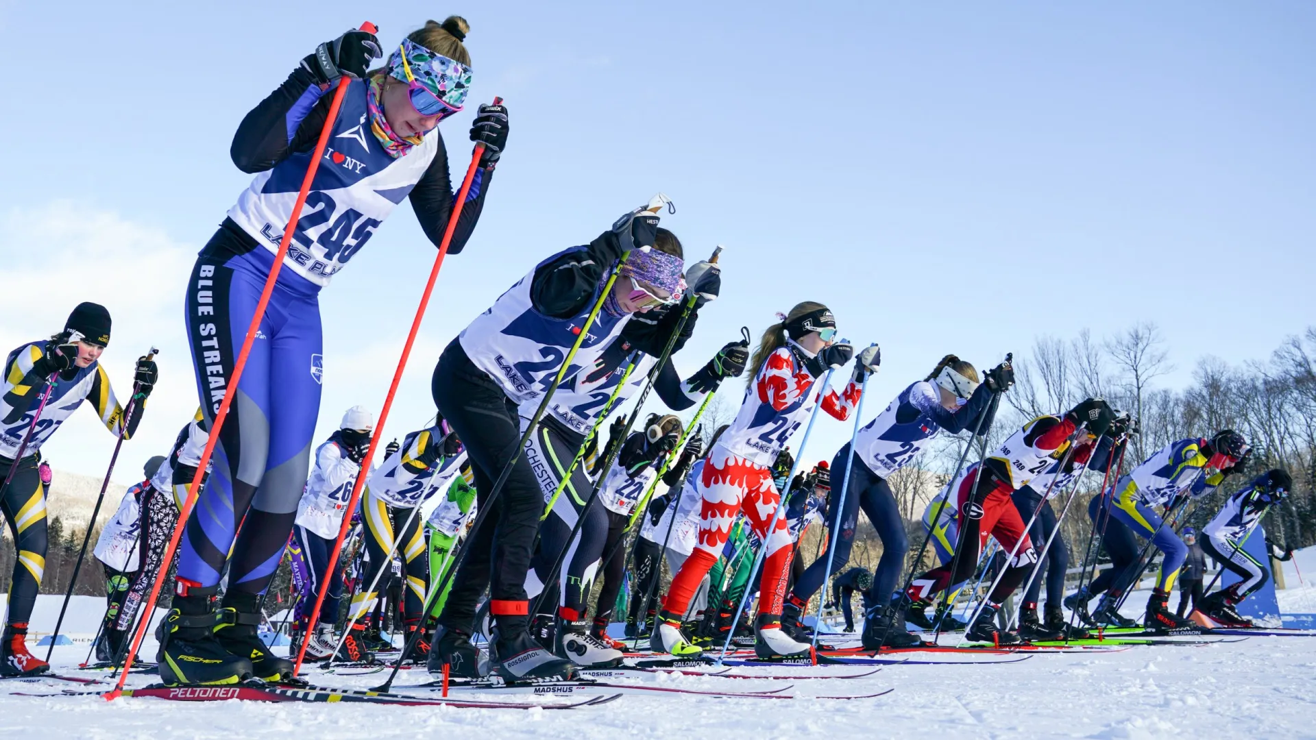 Competitors lined up for a cross-country skiing race, showcasing various athletic outfits.