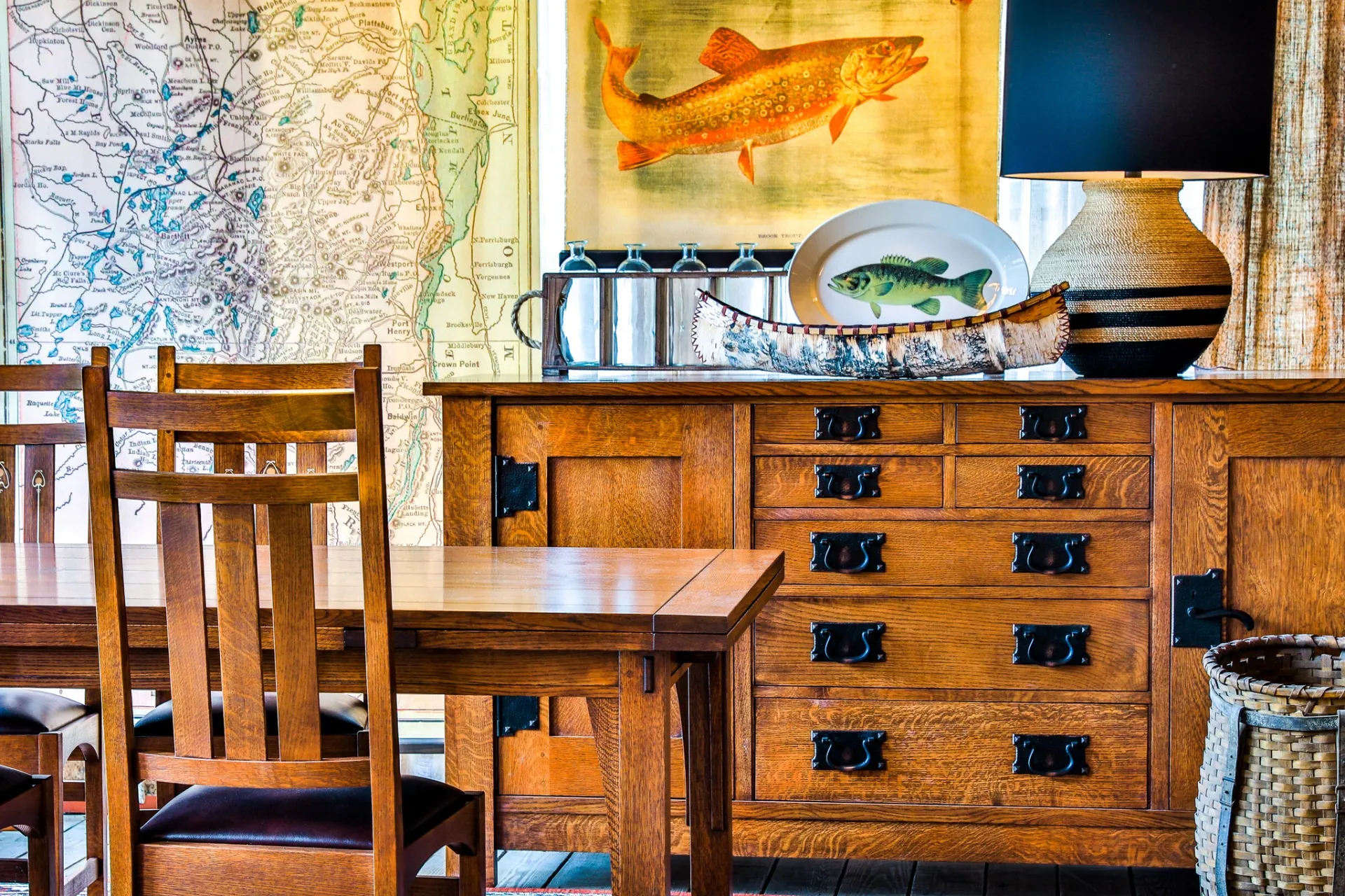 A table, dresser with maps and large art print of a fish on the wall.
