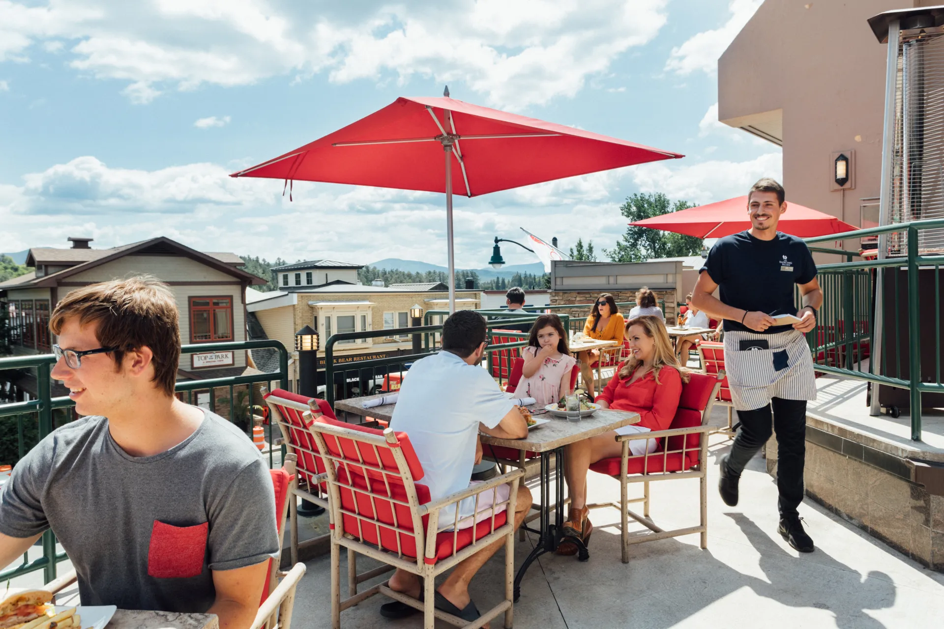 Couple sits at rooftop table with red umbrella in summer