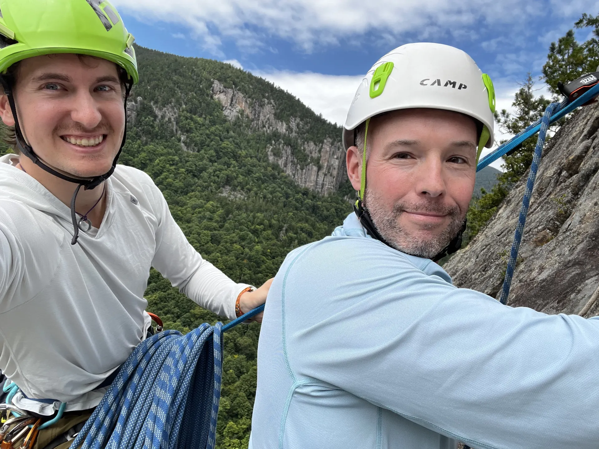 Two men smile into the camera while climbing a rock ledge