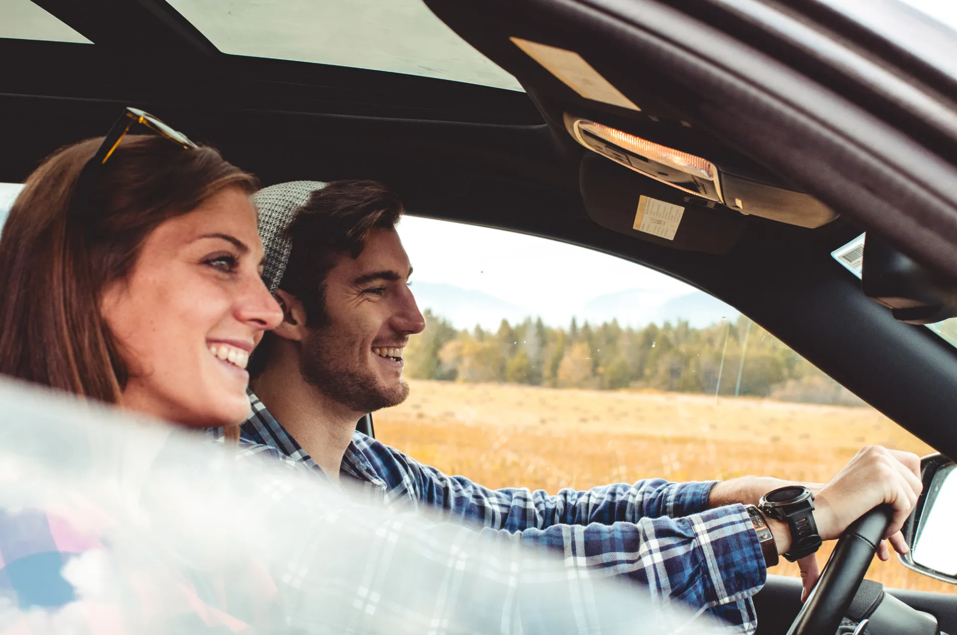 A couple driving a car with a scenic background behind them.