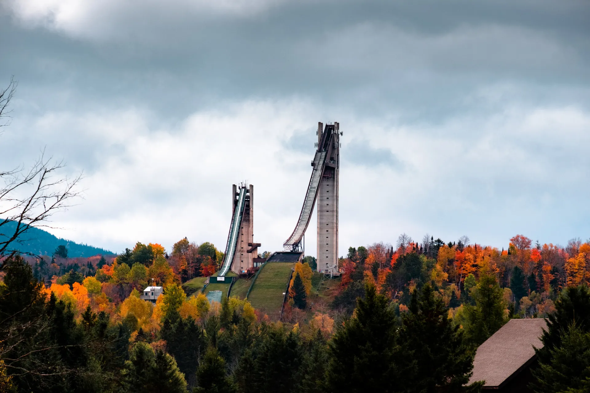 Two Olympic ski jumps tower over the trees on a mountain in fall.