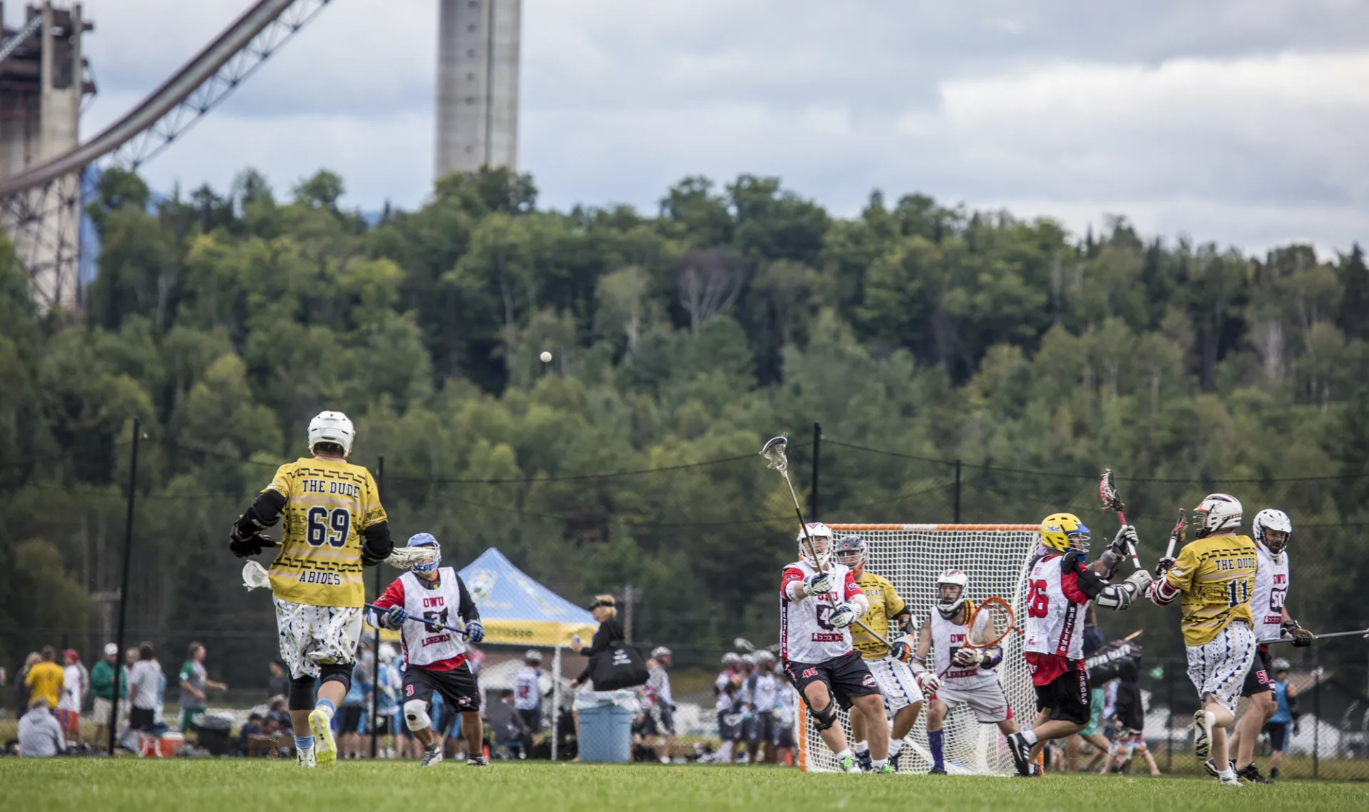 Players rush to the goal while spectators sit around the field in the shadow of the Olympic Ski Jumps at the Horse Show Grounds in Lake Placid.