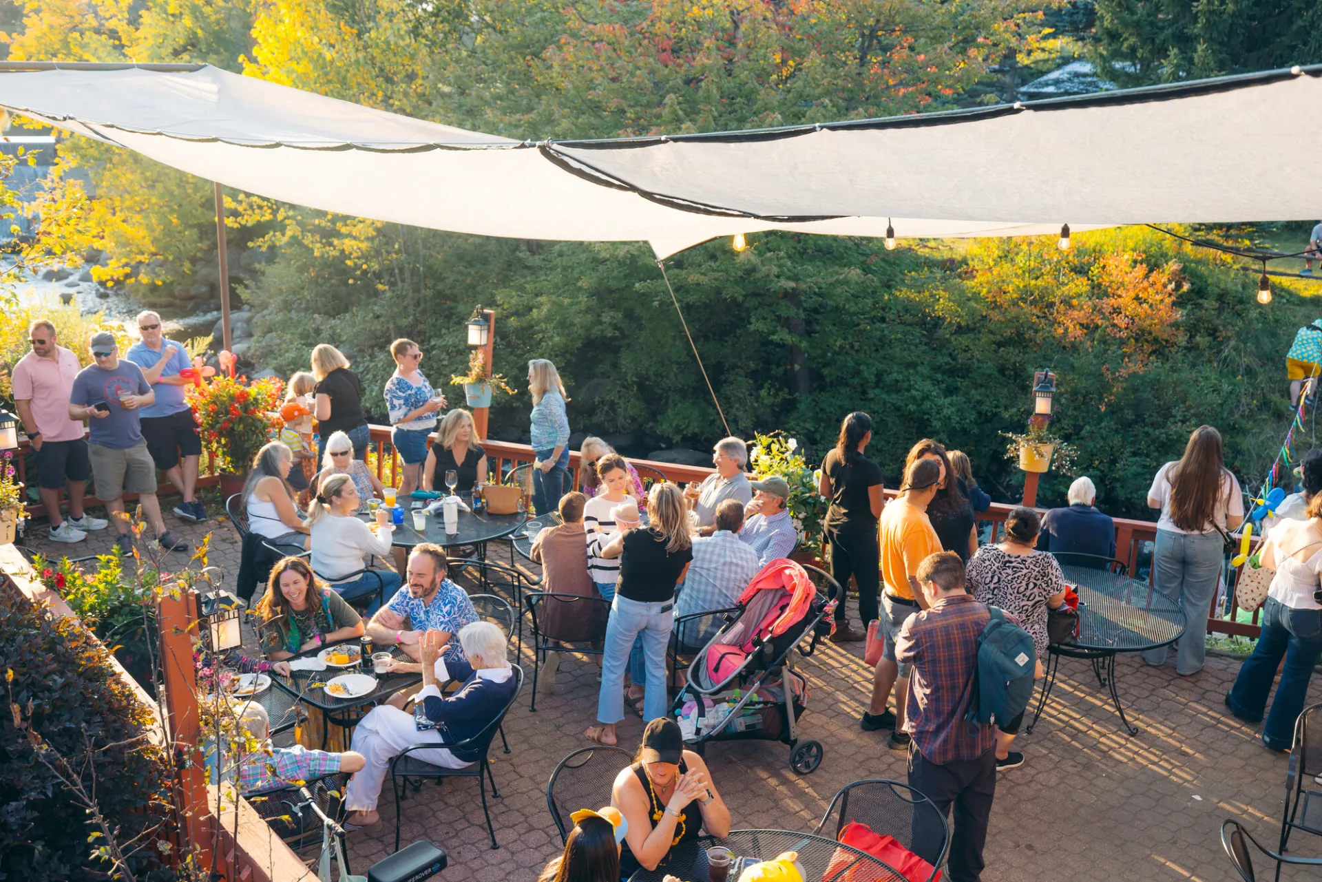 Crowd photographed from above on canopied outdoor patio sitting at tables and standing, some wearing duck accessories 