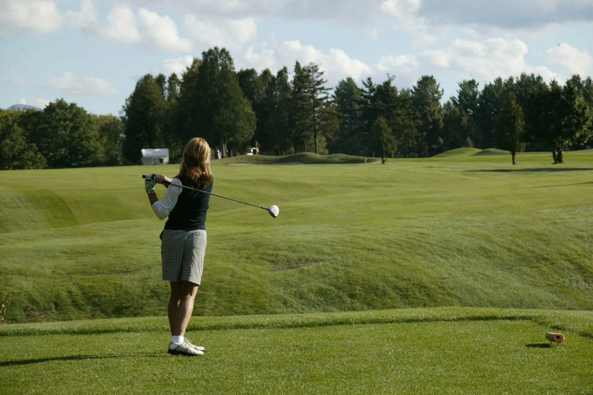 Woman in golf attire stands in backswing with golf club on green of Whiteface Club & Resort golf course