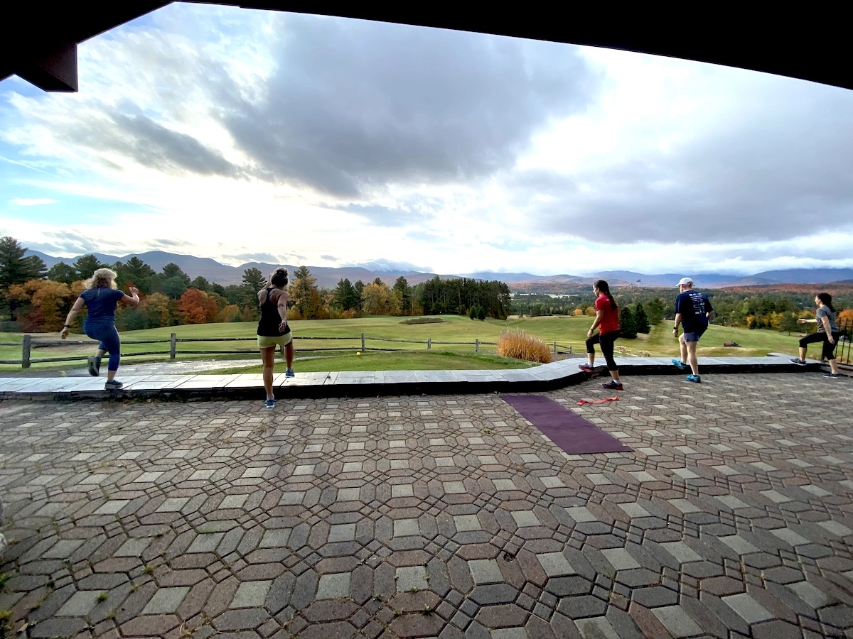 Five people participate in an outdoor fitness class on a patio overlooking a golf course and mountains.