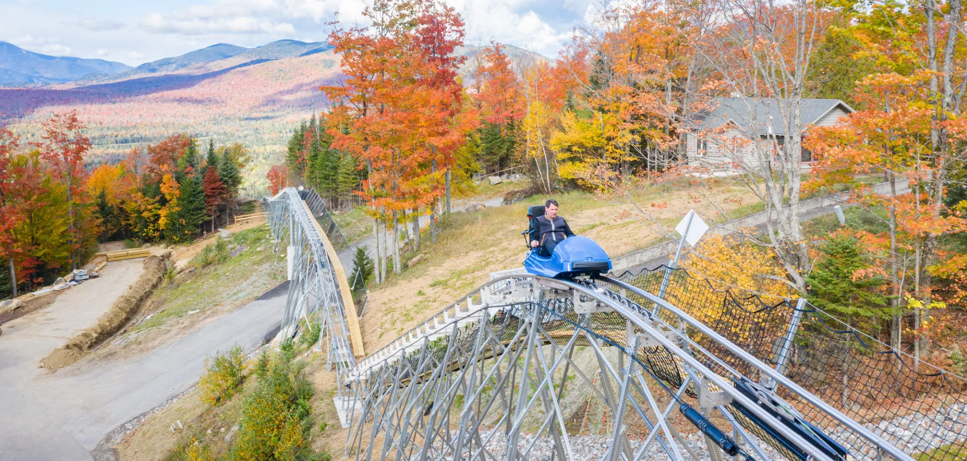 Man rides mountain roller coaster with fall foliage and mountains in background