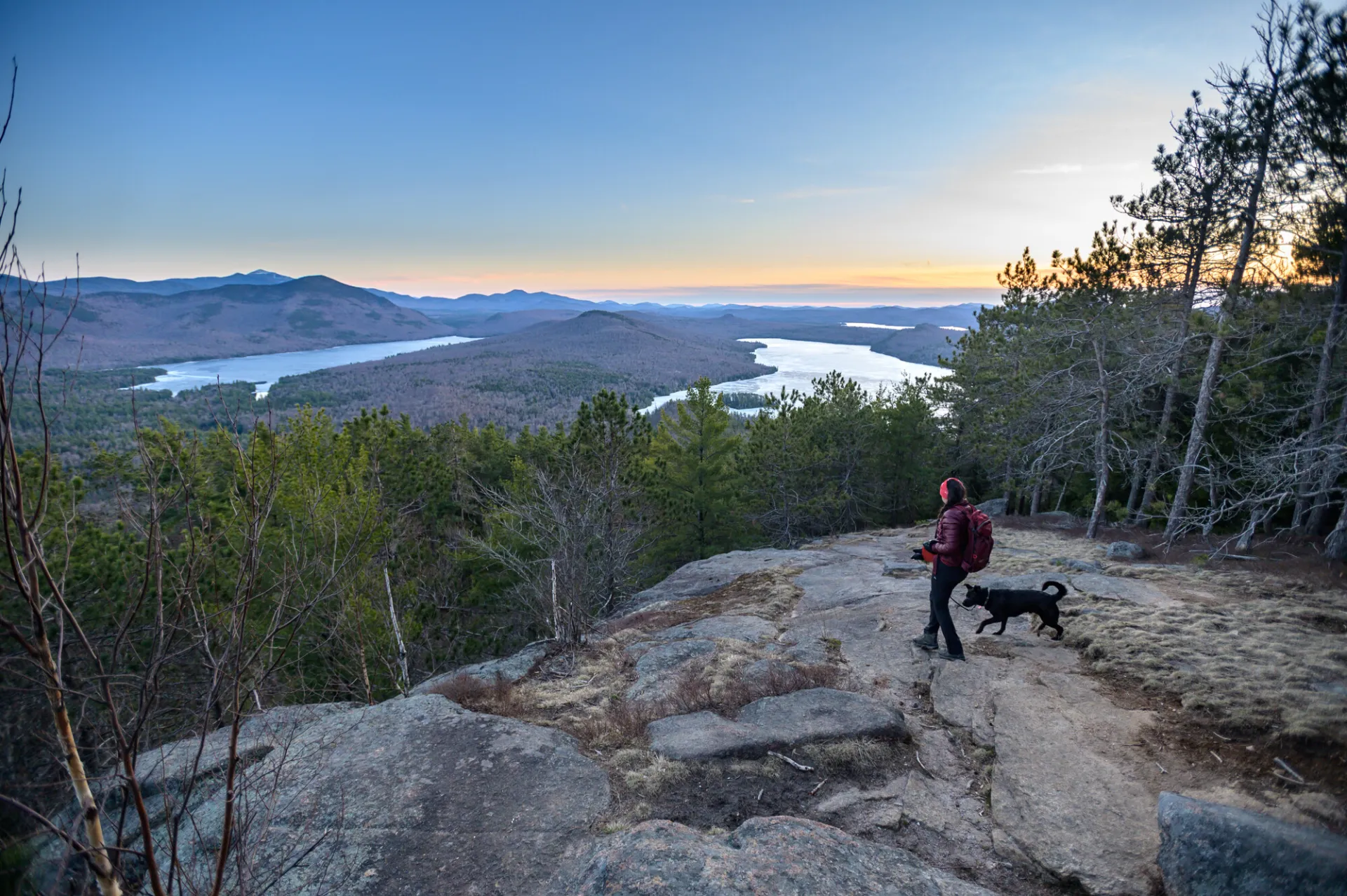 A hiker and her dog standing at the summit of a hike during the spring.
