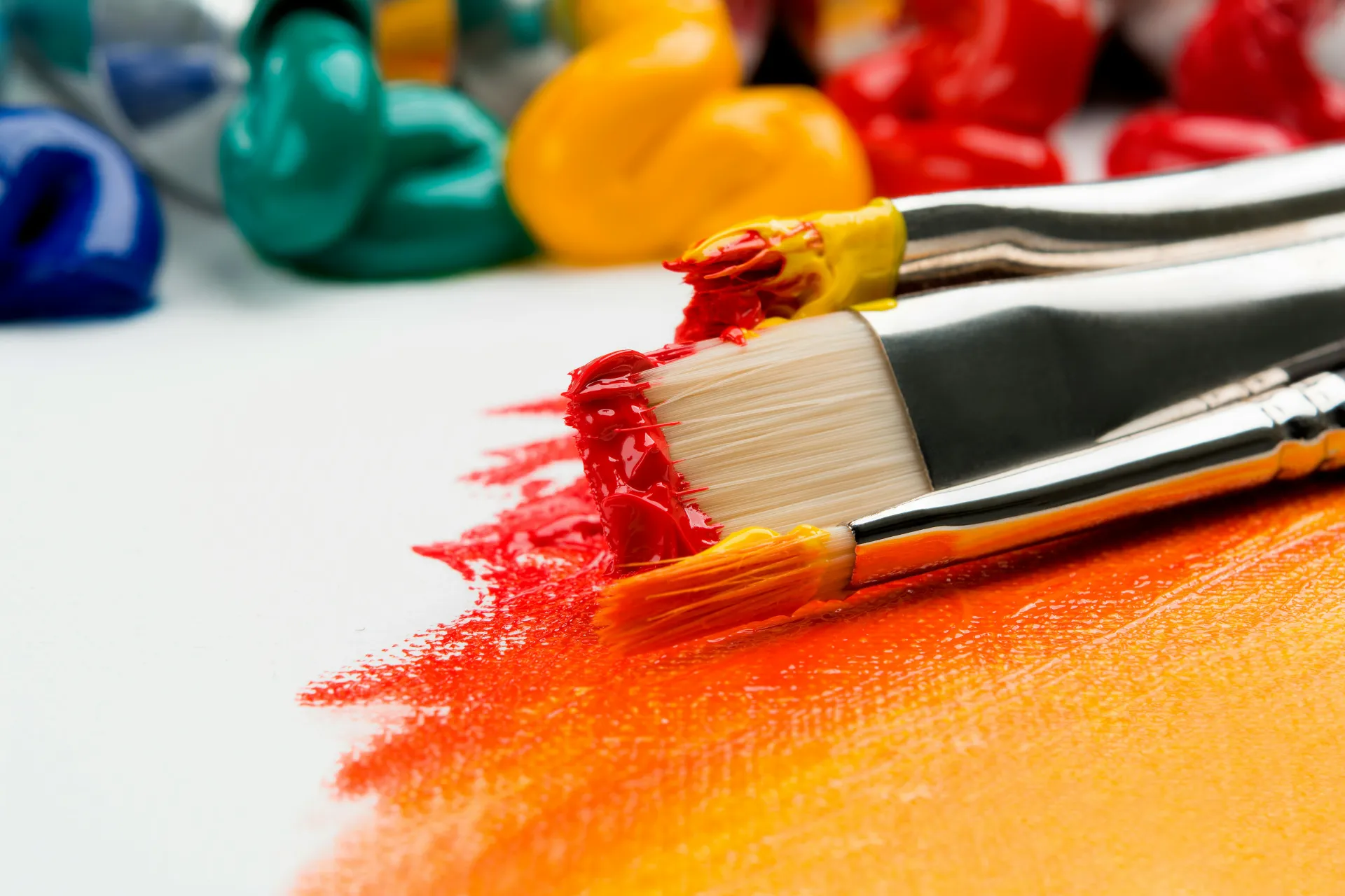 Stock image of paint globs on canvas with reds and oranges painted and paint brushes covered in paint.