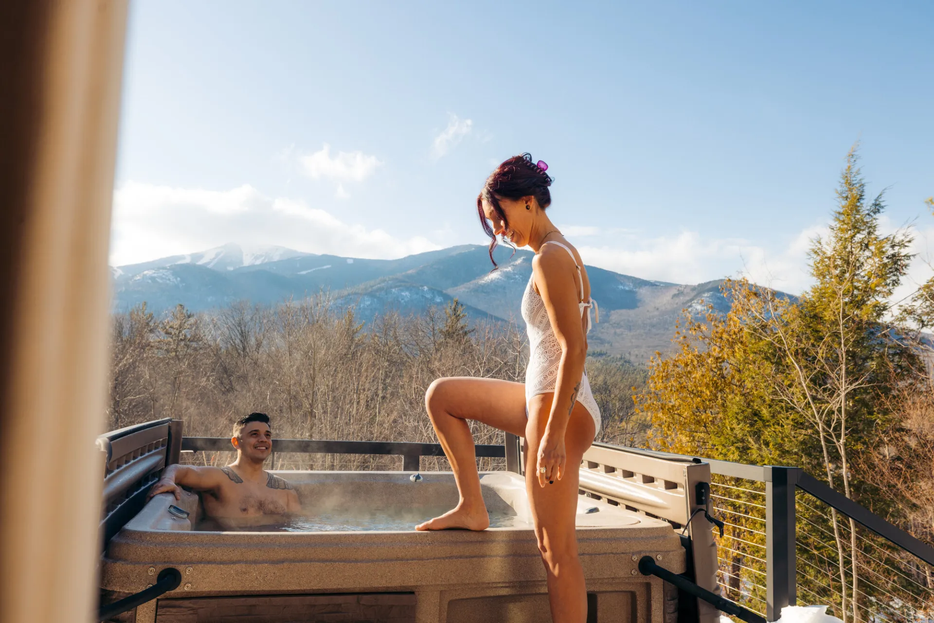 A man and woman enjoy a hot tub at a mountain cabin.