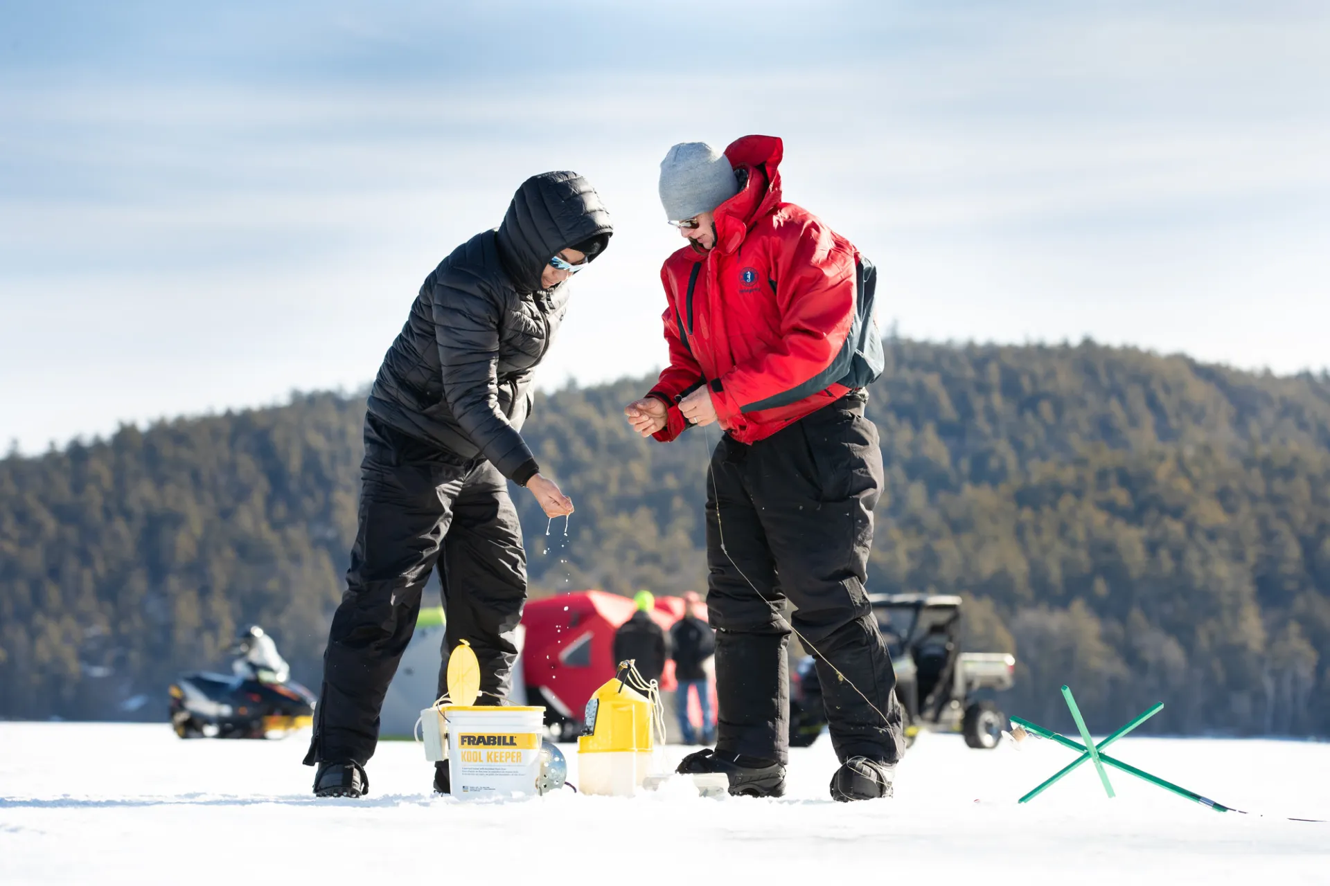 Two people use an augur on a frozen lake