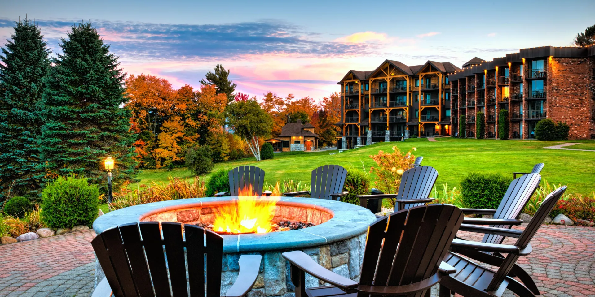 A stone fire pit ringed with adirondack chairs in the front lawn of Lake Placid Club Grandview