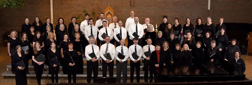 A large choir group, dressed in black and white formal attire, poses for a group portrait on tiered risers inside a church.