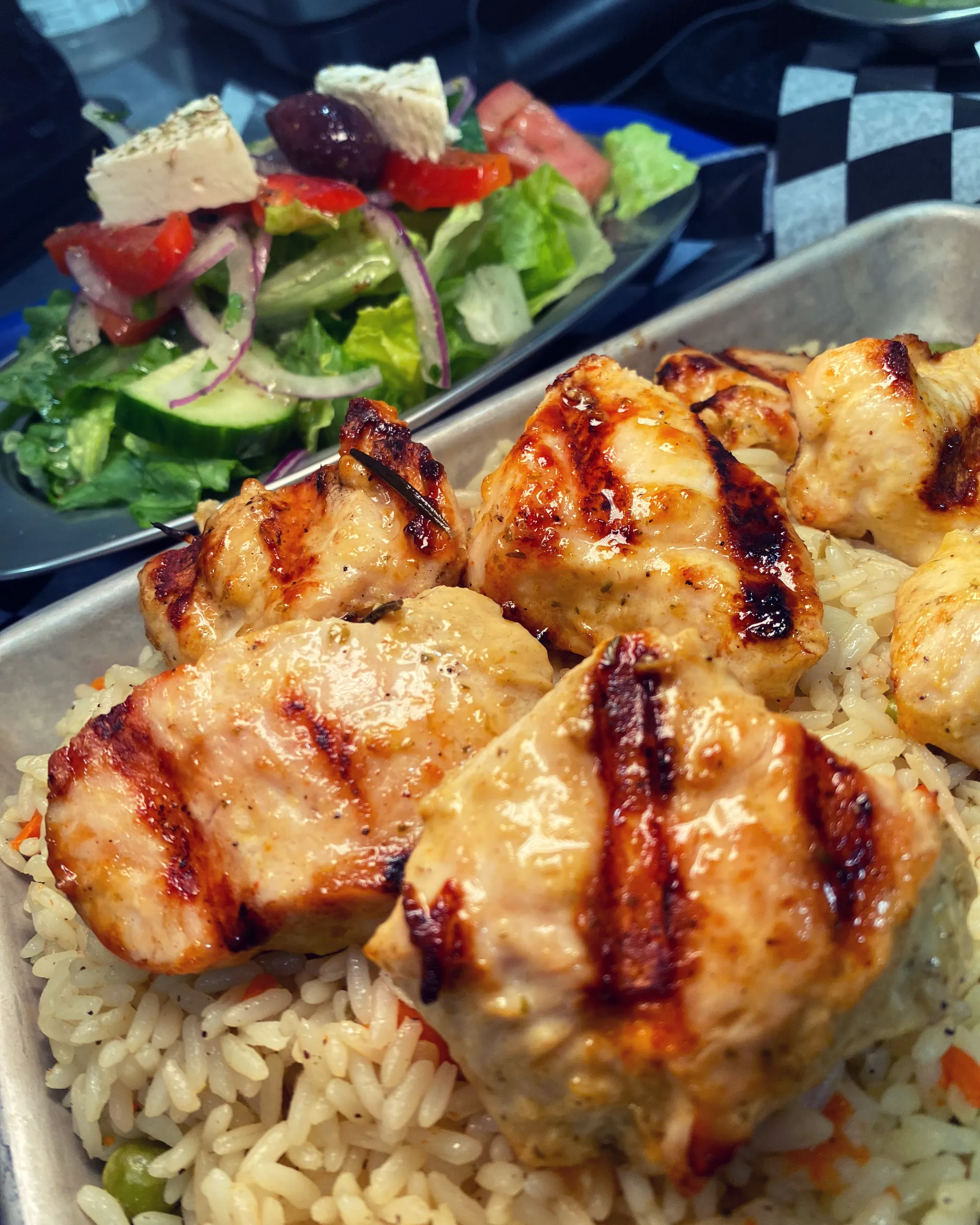 Rice topped with grilled chicken with a fresh salad behind.