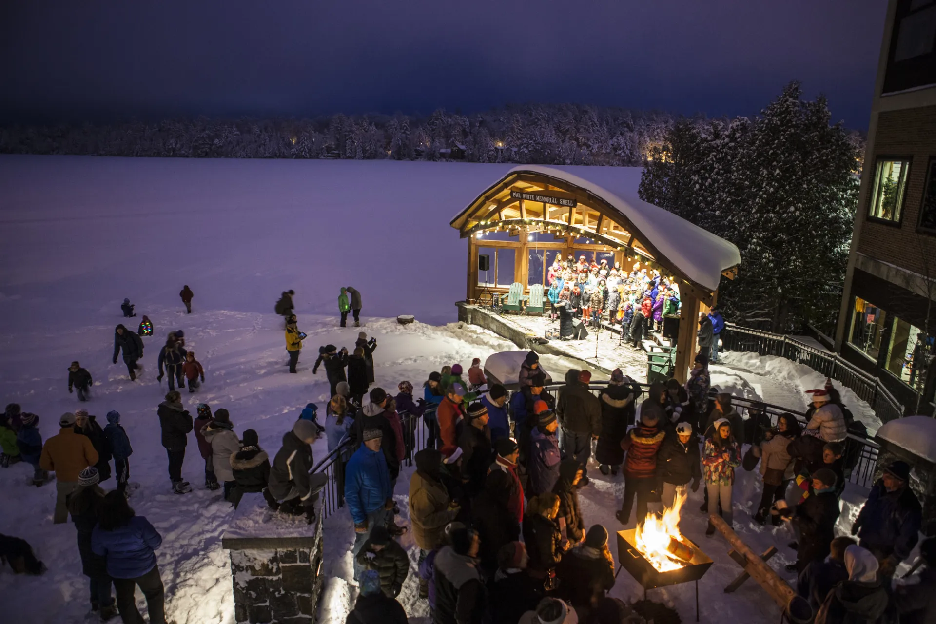 A winter concert on Mirror Lake in Lake Placid with a snowy backdrop and a crowd of people.