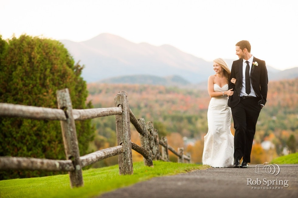 Bride and Groom walk the fence line with the fall foliage illuminating the mountains behind them.