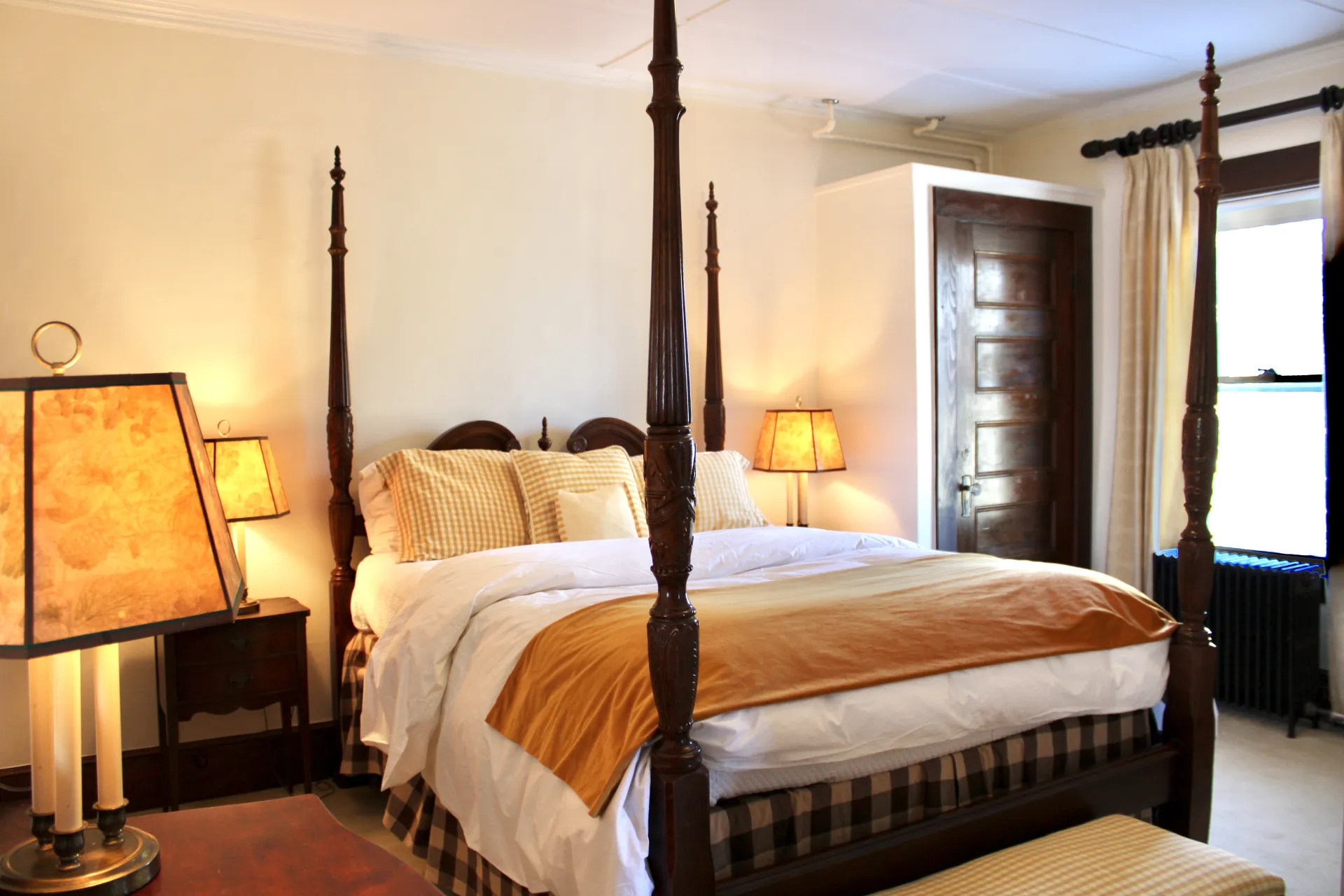 A dark four poster bed with cream colored bedding.