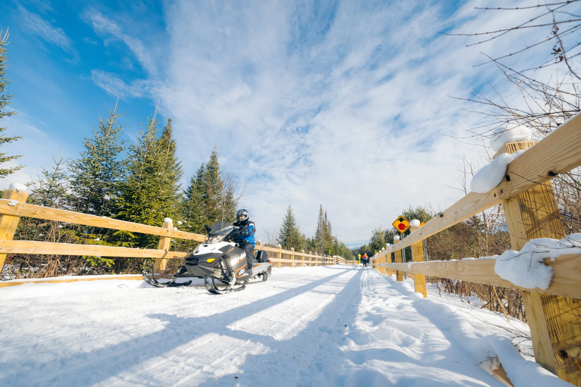 Snowy path with a person riding a snowmobile on a sunny day in Lake Placid, NY.