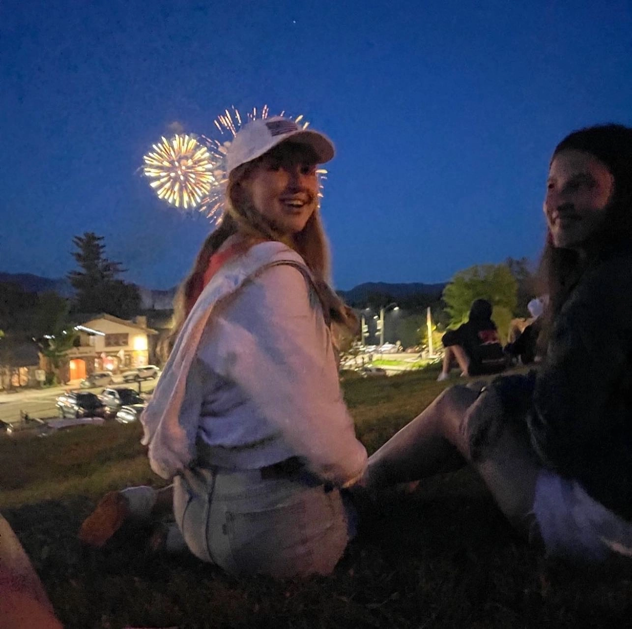 A young woman smiles as fireworks light up the sky behind her.