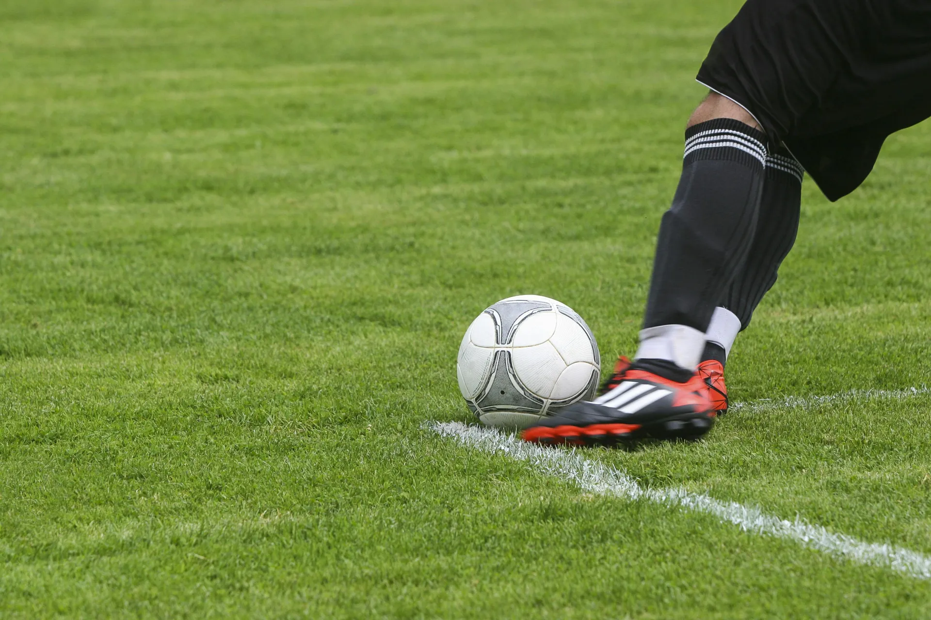 Cleated foot seen kicking a soccer ball on a green field with white lines
