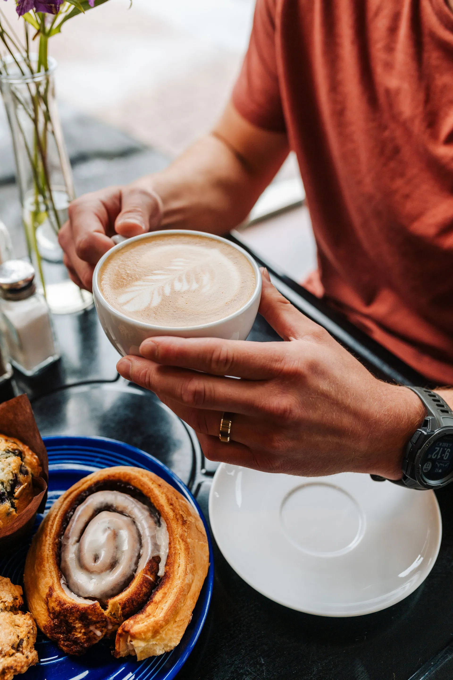 A pair of hands holding a latte with cinnamon buns.