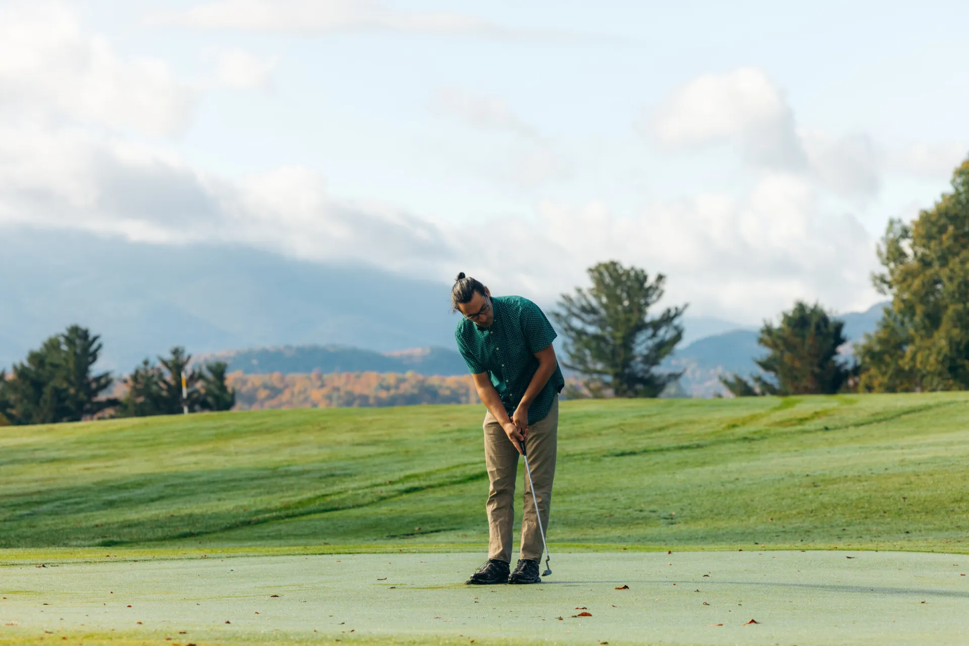 A golfer putting a ball on the green with mountain vistas in the background.