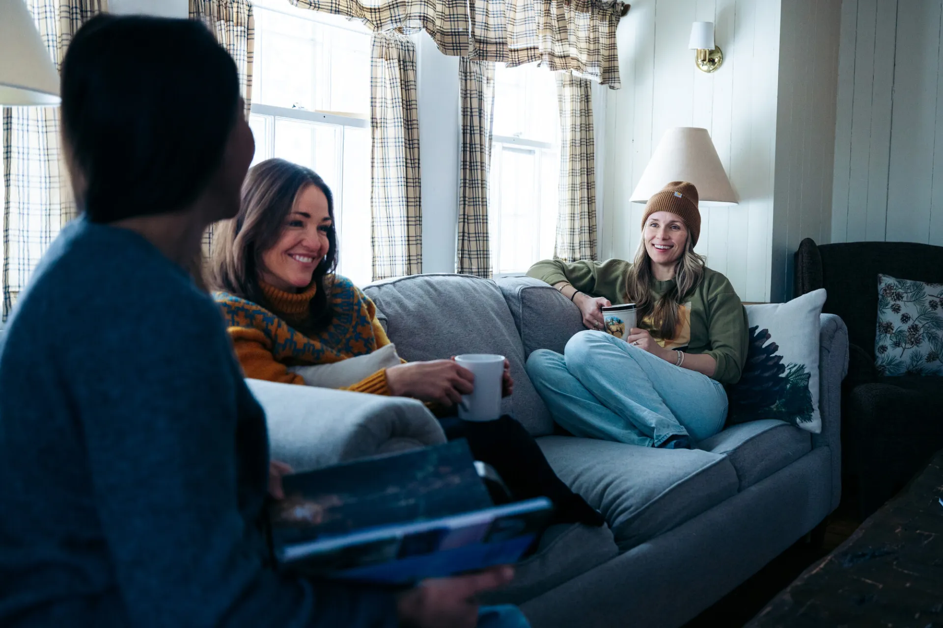 A group of three women talk on a couch in a cottage.