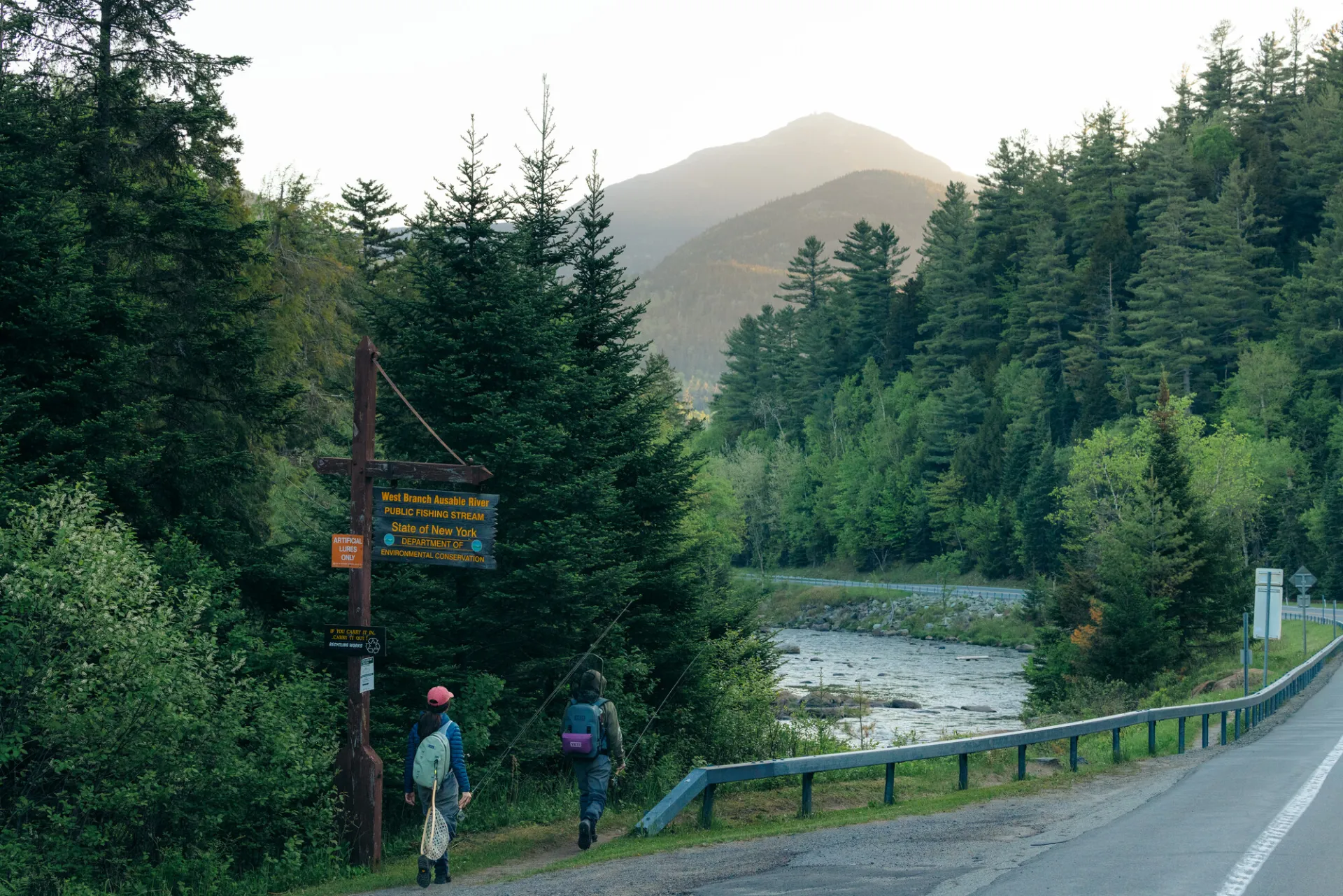 Two fly fishers walk towards a roadside river