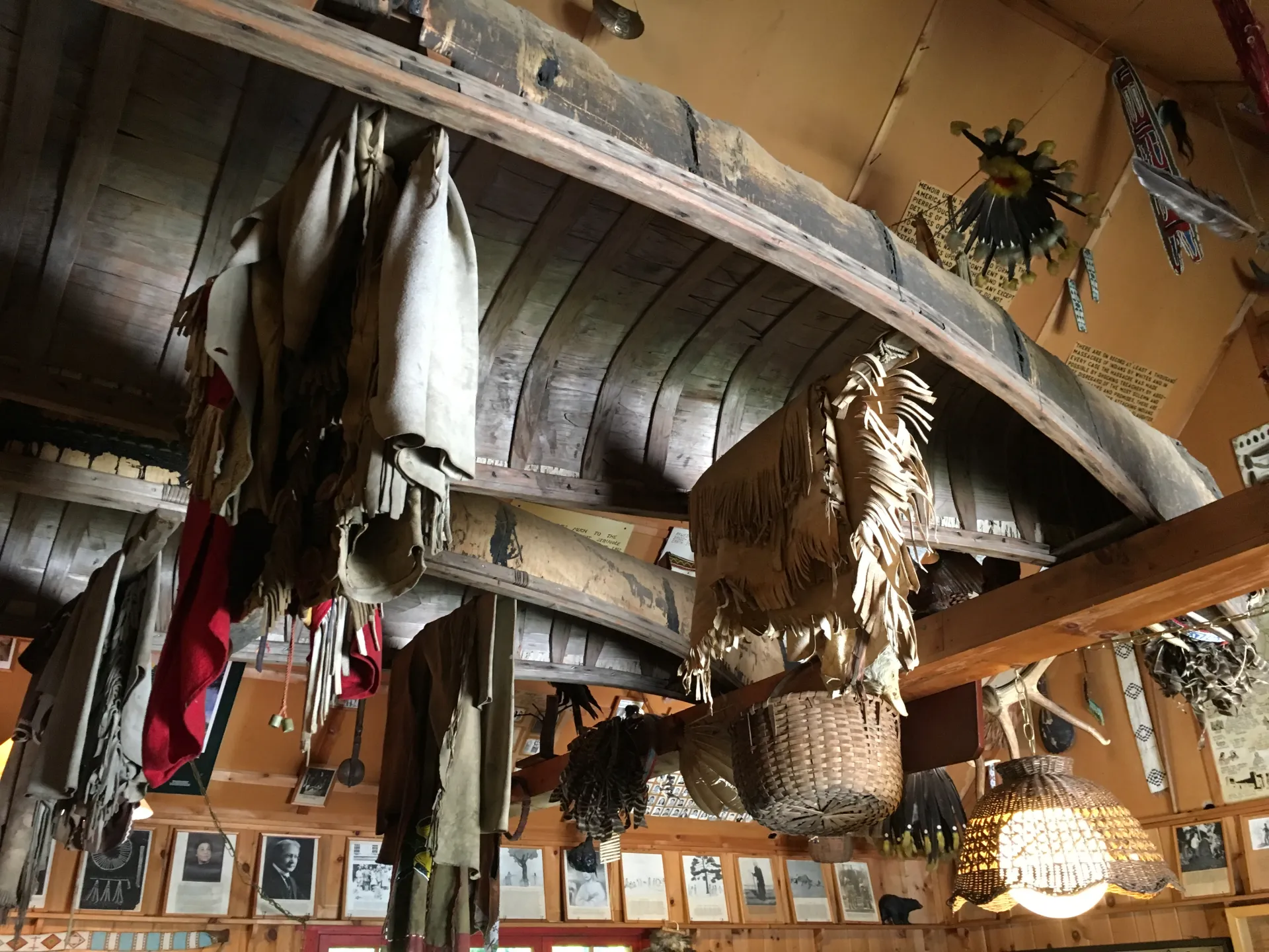 An old Indigenous canoe hangs from the rafters of a museum ceiling, among other items, including baskets.