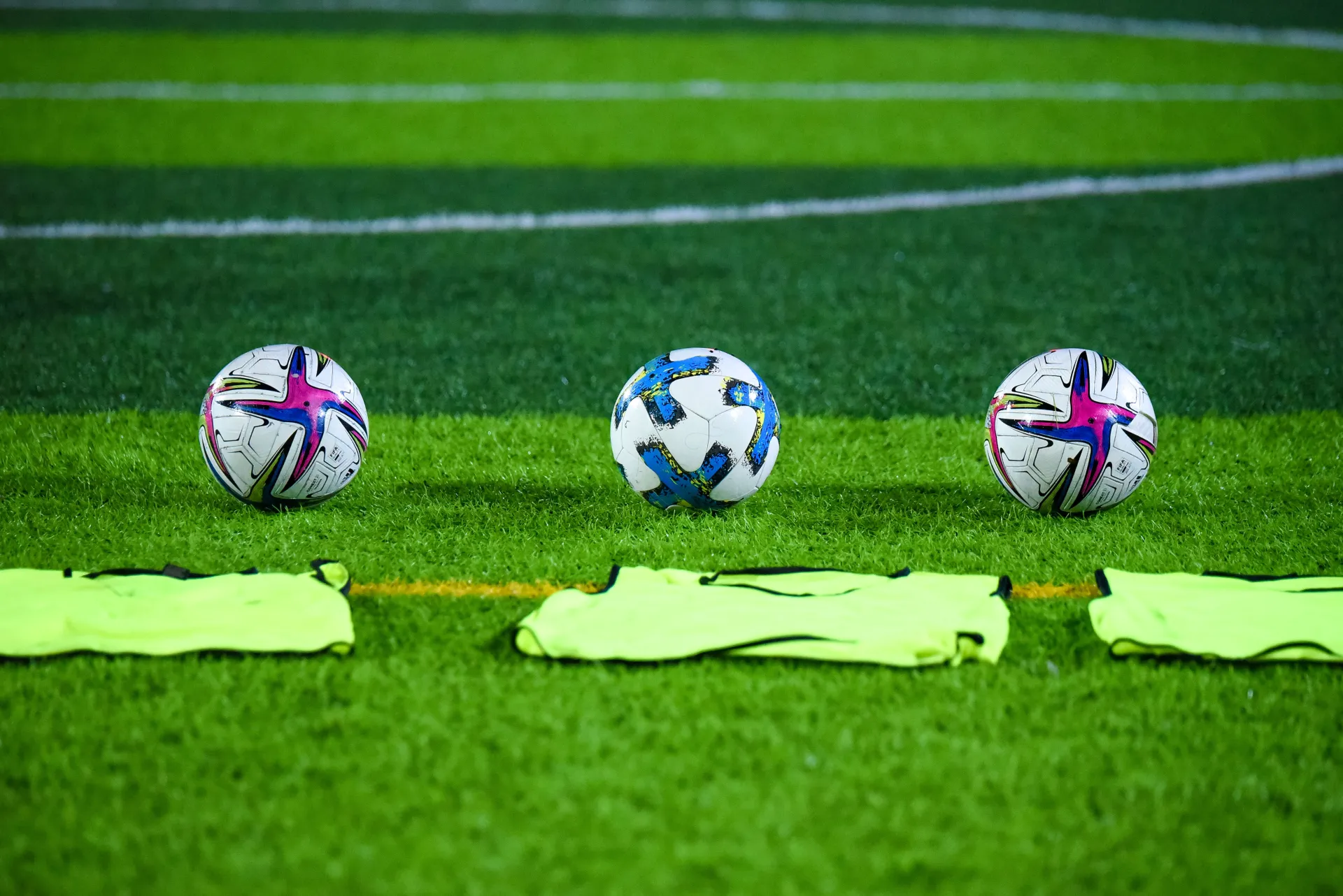 Three soccer balls on green soccer field with green pinnies laying on the ground in front of them