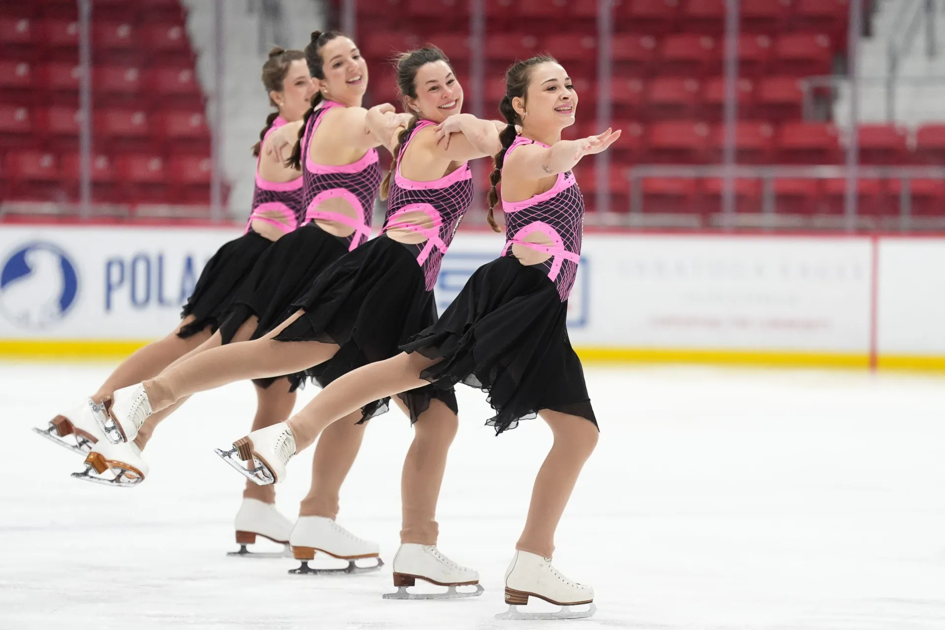 A synchronized ice skating team performs a routine in matching outfits, showcasing graceful movements on the rink.