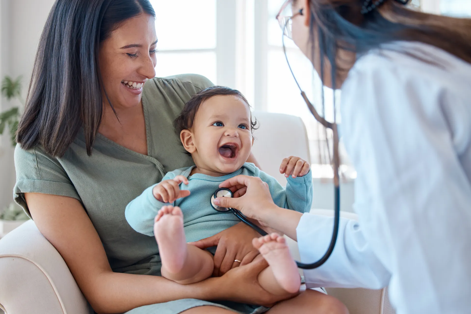 A woman holds a baby as a doctor listens to her heartbeat.