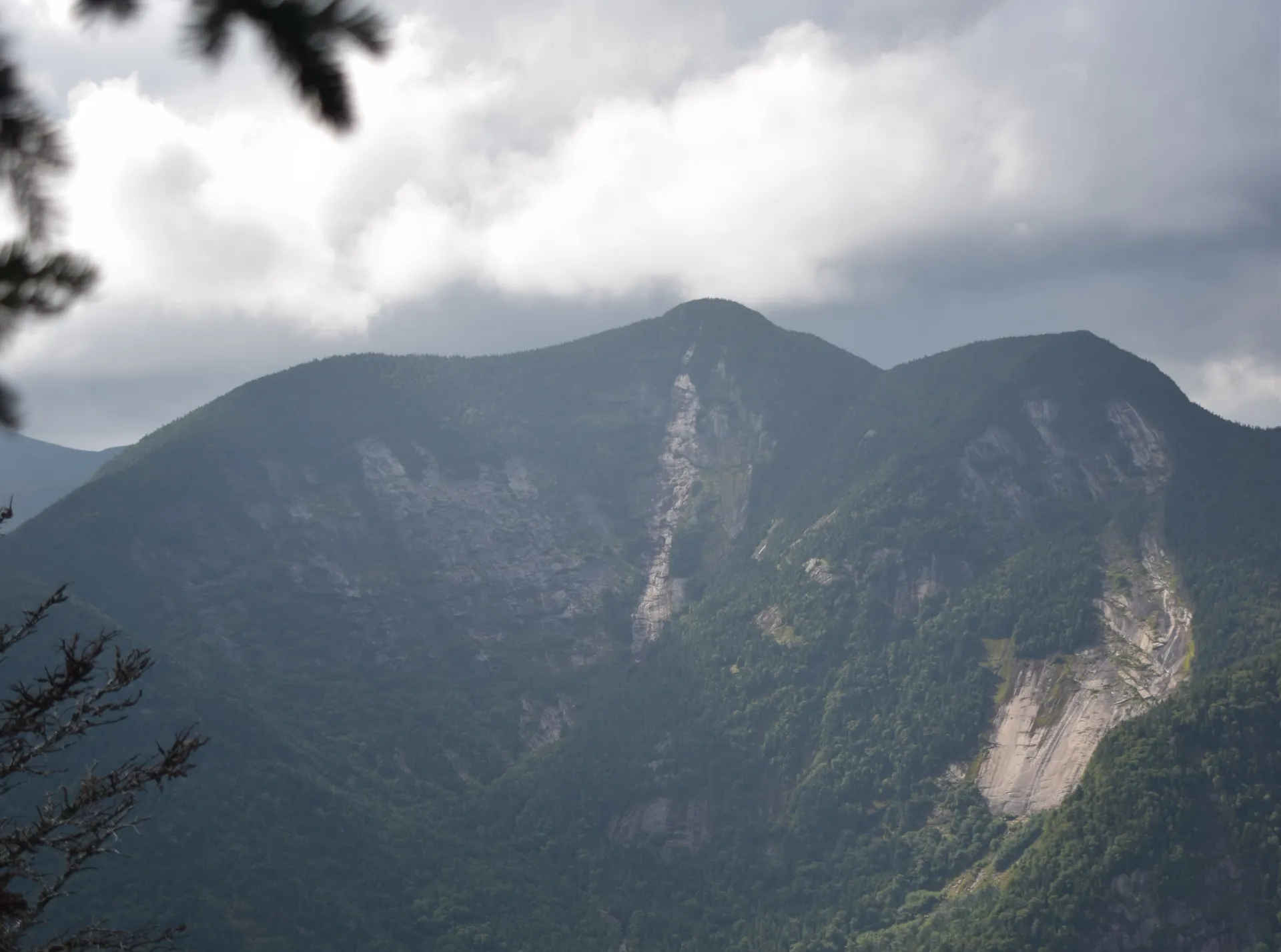 A through-the-trees view of a tall, three-peaked mountain
