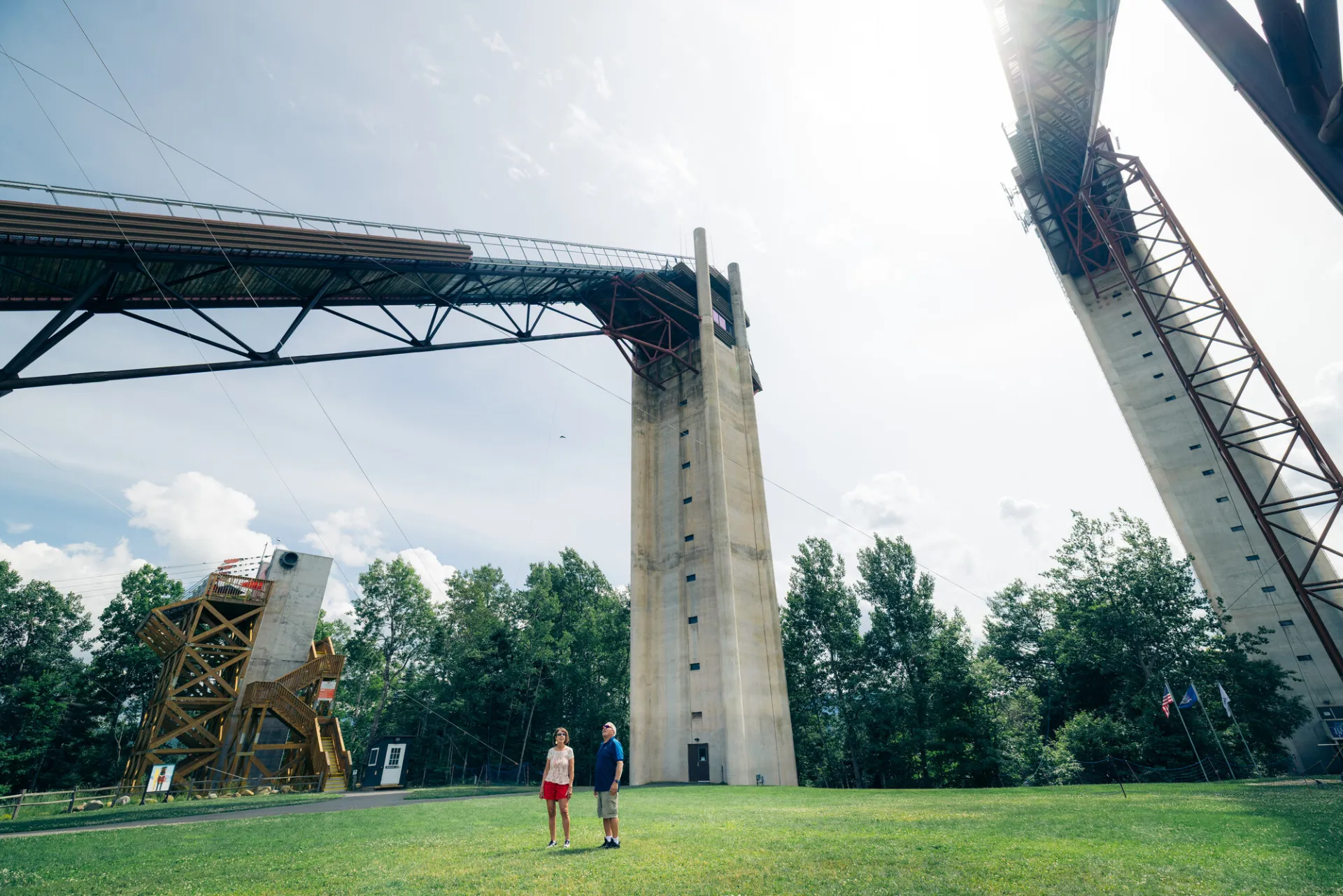 Senior couple stands on grass at the base between two towering ski jumps