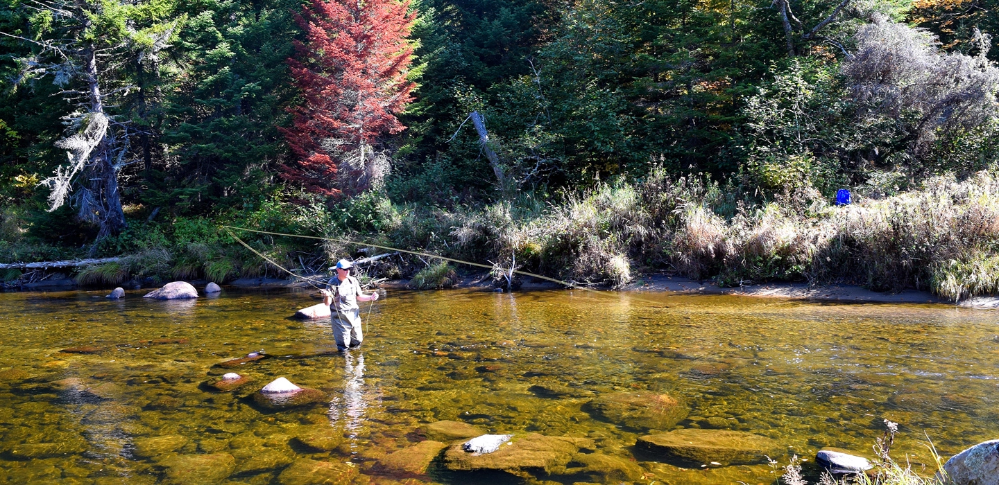 A person stands in the water while fly fishing.