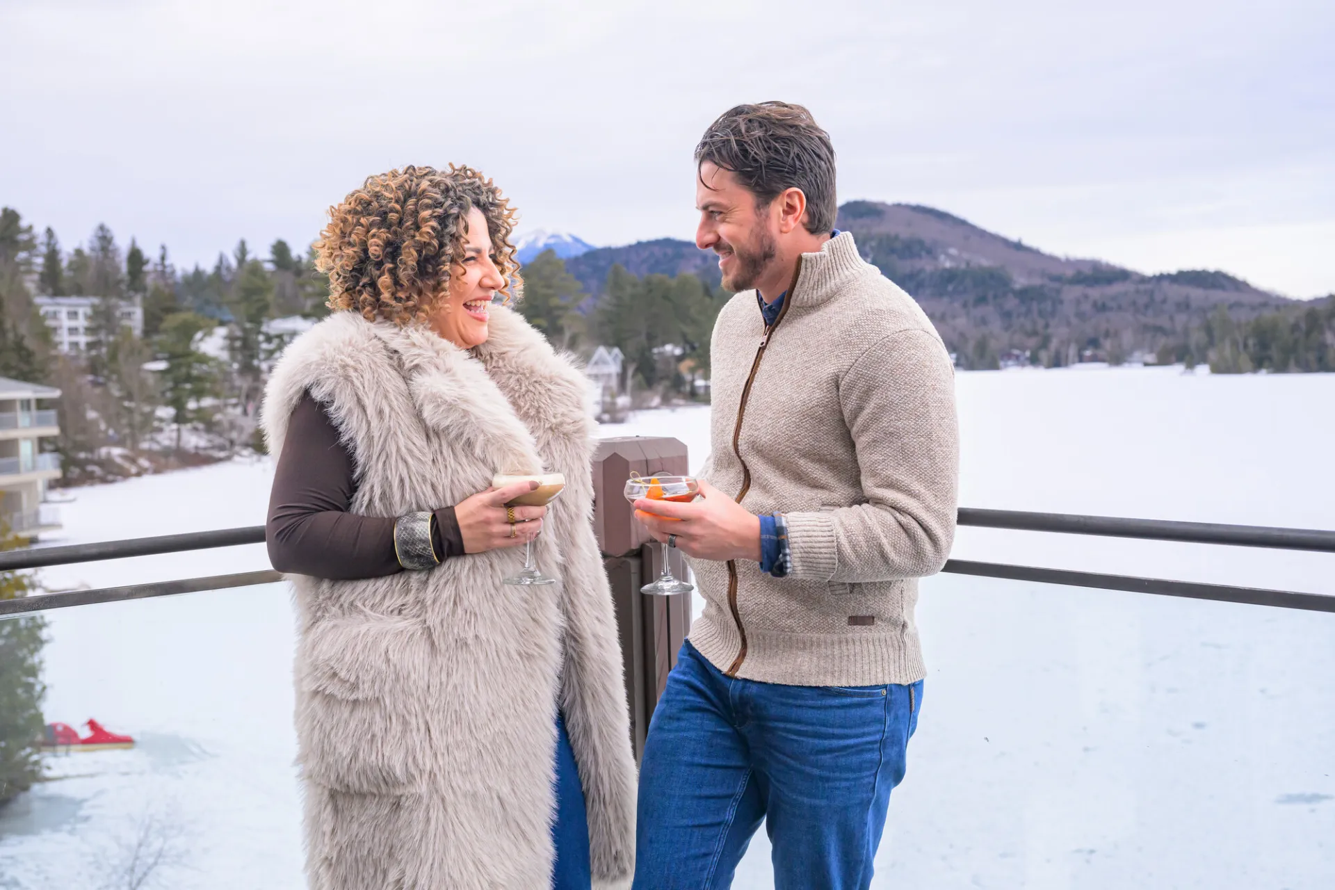 A couple standing on the patio at Top of the Park with cocktails and winter scenery behind them.