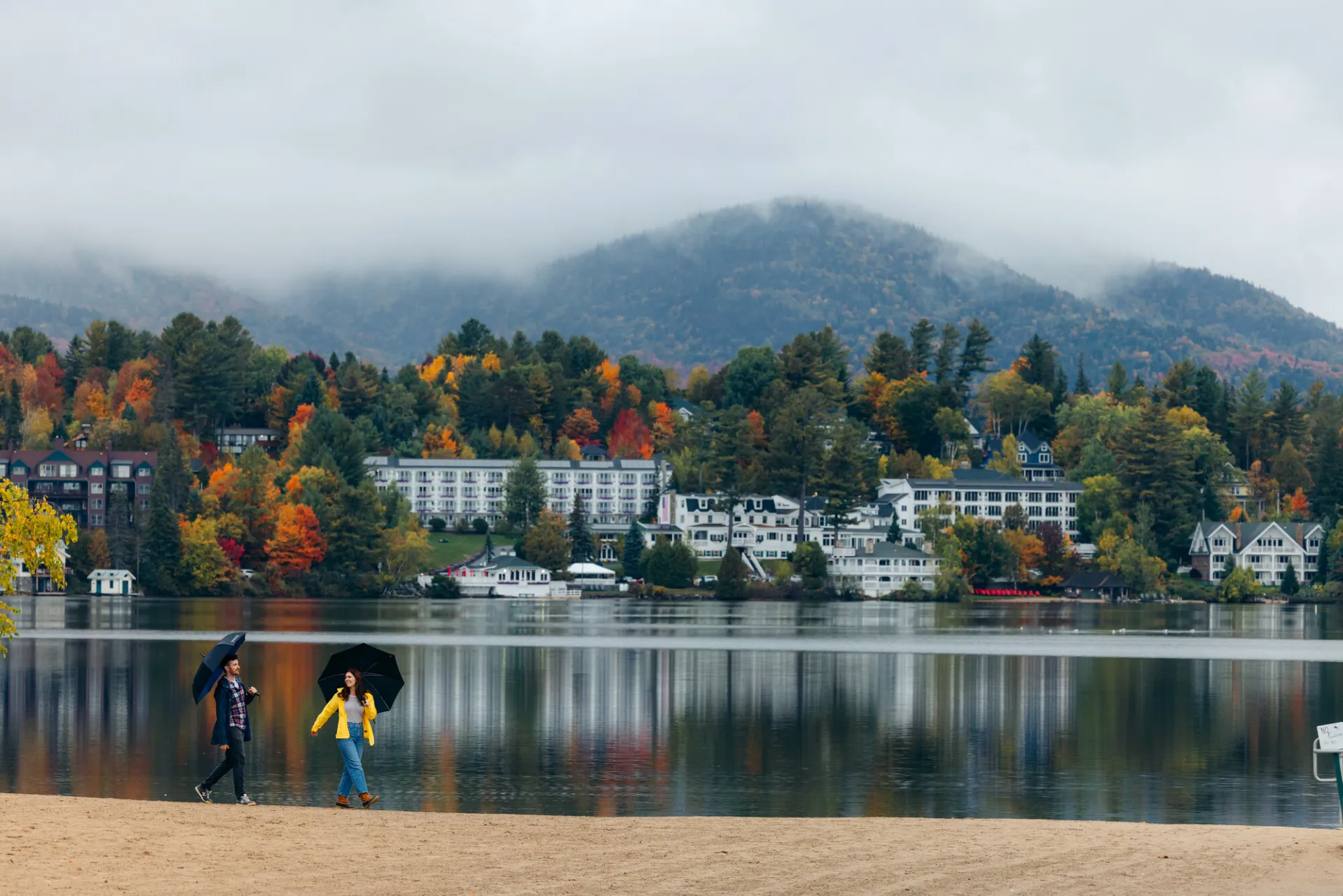 A man and woman walk on a beach on a foggy day in a small mountain town.